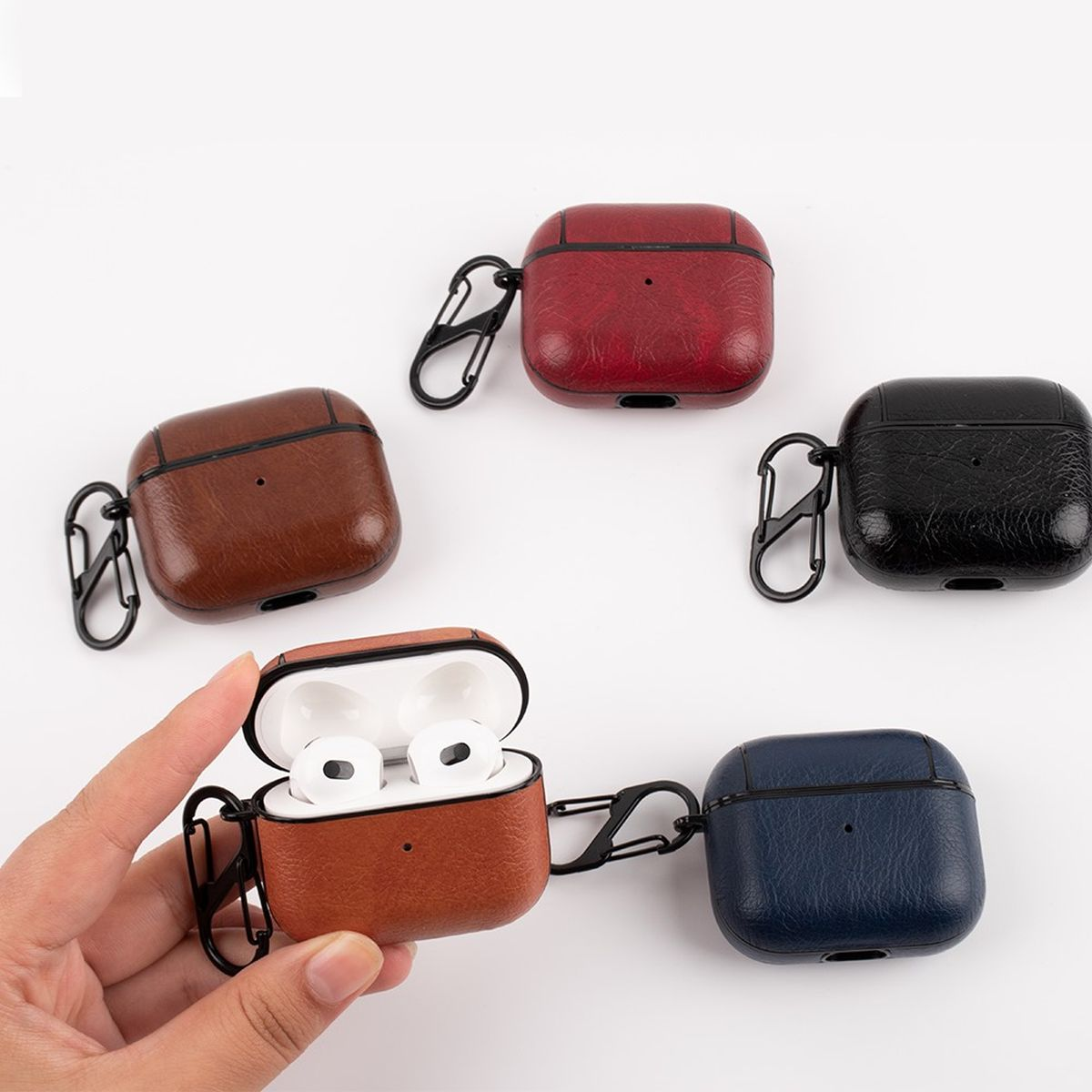 Vier lederartige AirPod-Hüllen in Rot, Braun, Schwarz und Blau mit einer Hand, die eine Hülle hält.