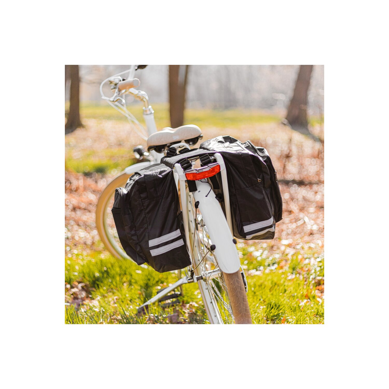 Ein Fahrrad mit schwarzen Packtaschen auf einem grasbewachsenen Weg mit Bäumen im Hintergrund.