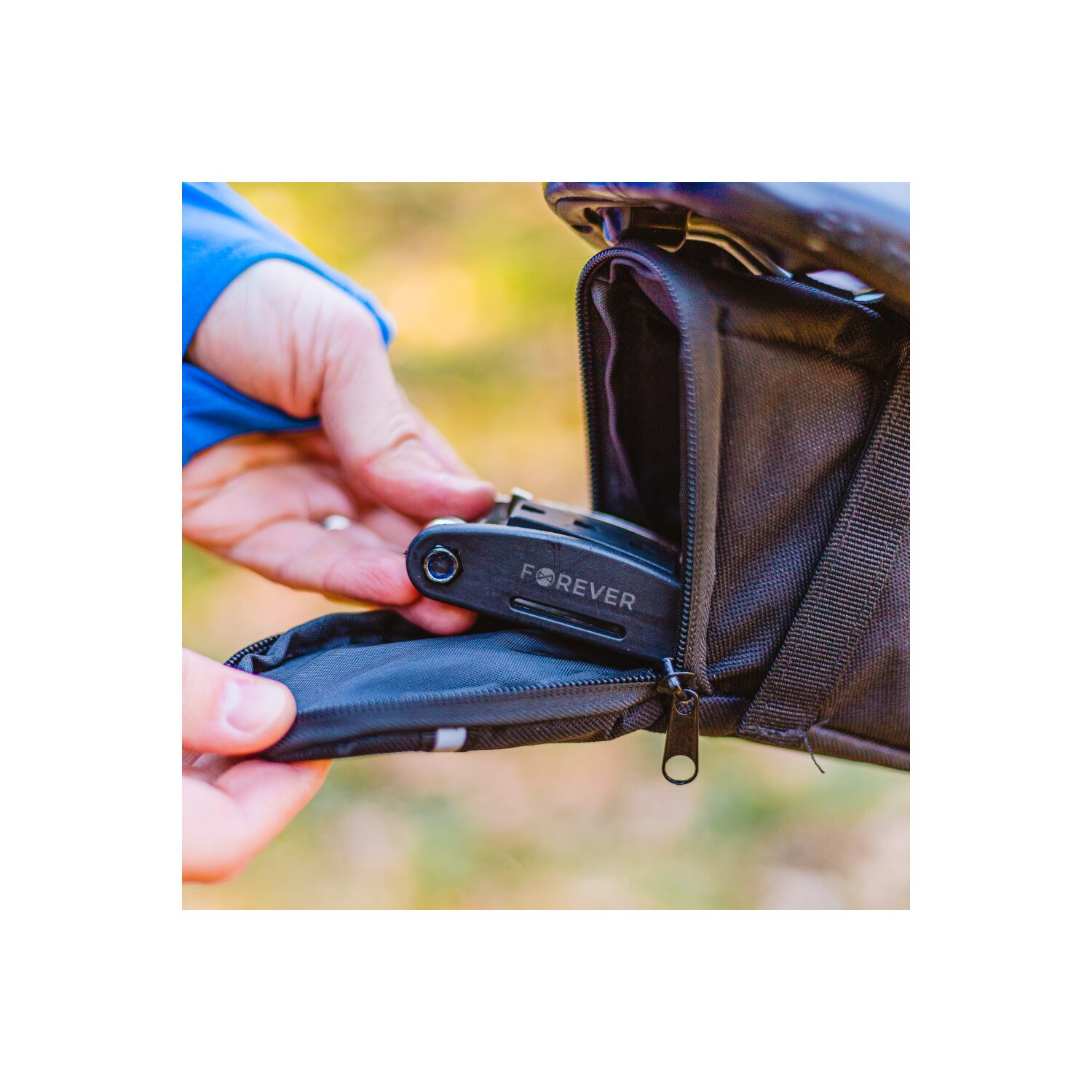Eine Hand nimmt Werkzeug aus einer schwarzen Tasche am Fahrradsattel.