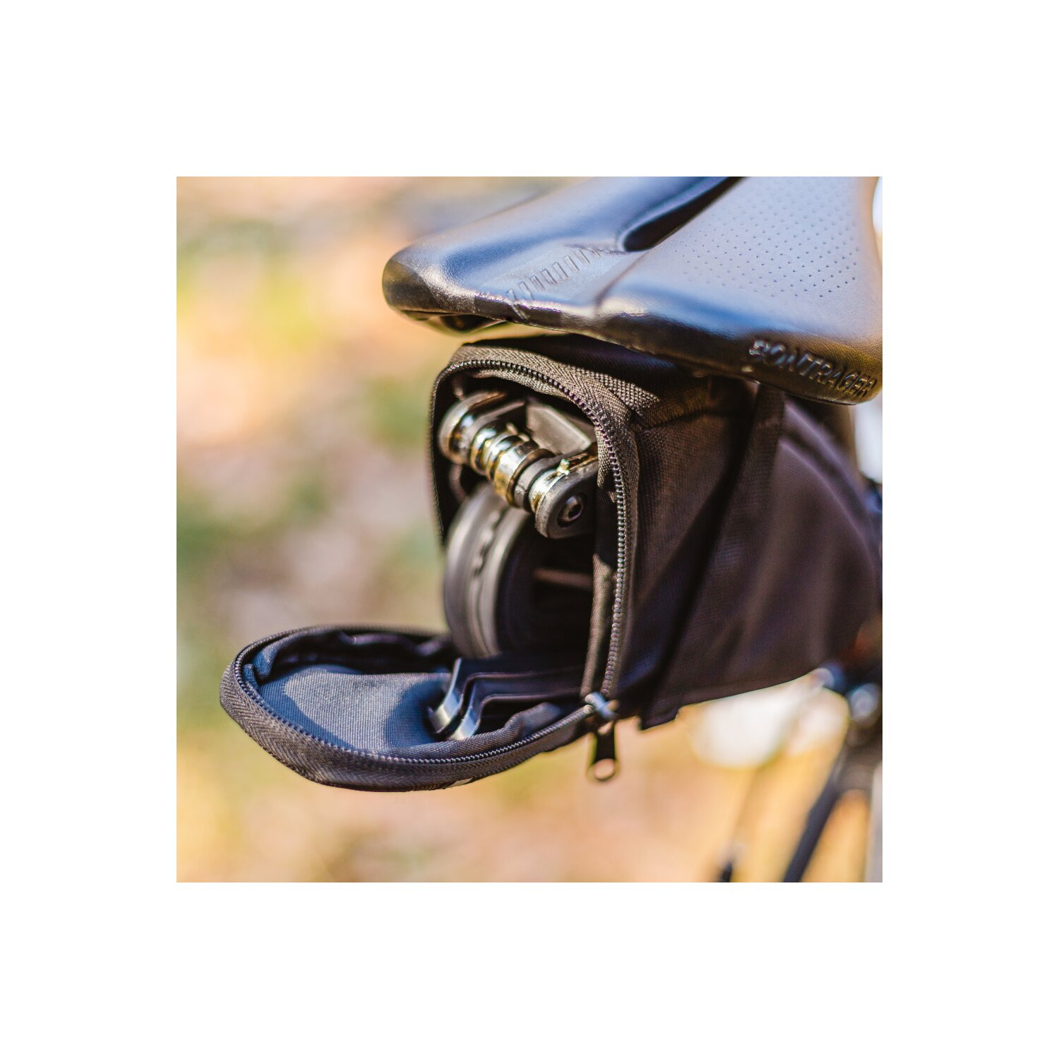 Schwarze Satteltasche mit Werkzeug, das an einem Fahrradsattel befestigt ist.