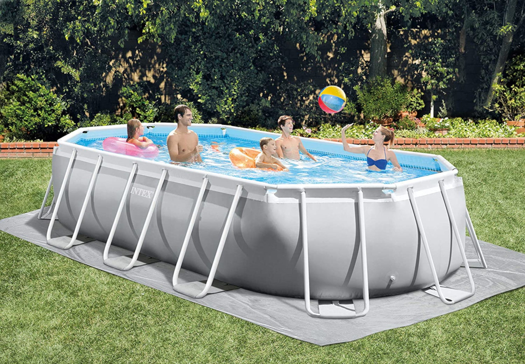 Ein rechteckiger Pool mit Leuten darin, in einem Garten mit Gras und Bäumen.