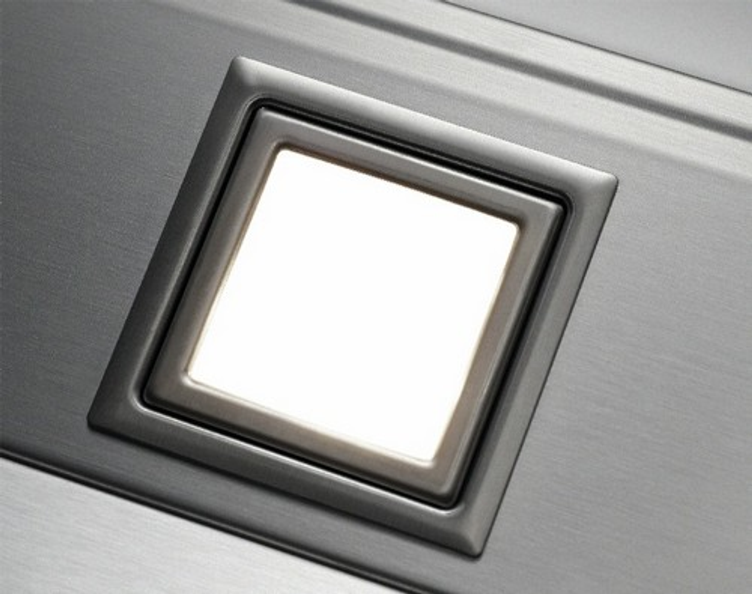 Close up of a silver light fixture recessed in a surface. The light is bright white.