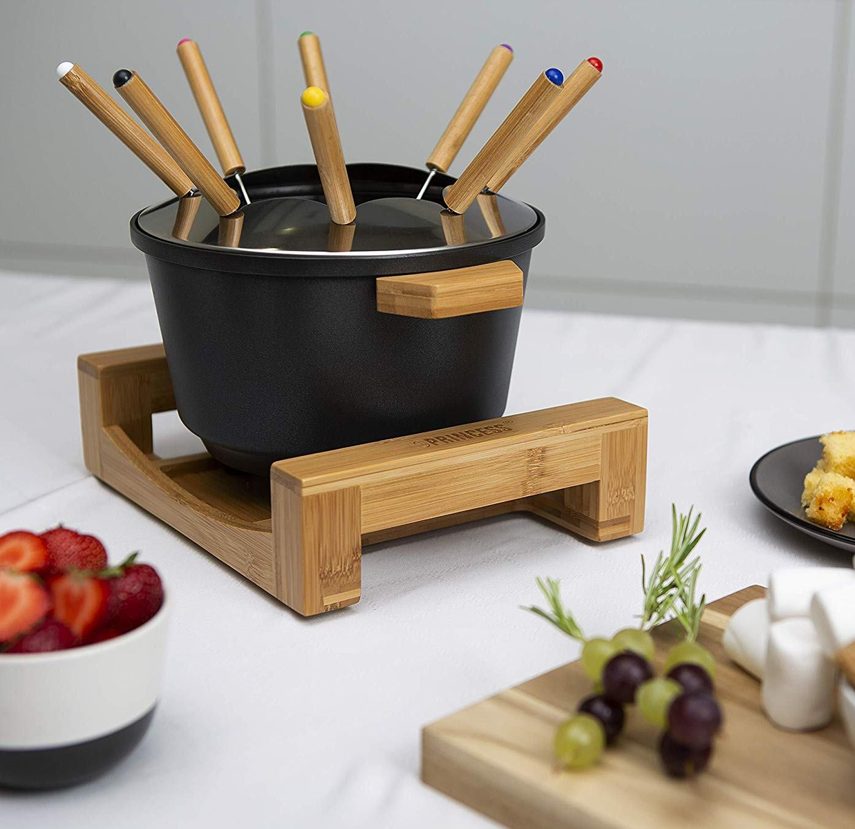 Zestaw do fondue z kolorowymi widelcami, truskawkami i winogronami na drewnianej desce.