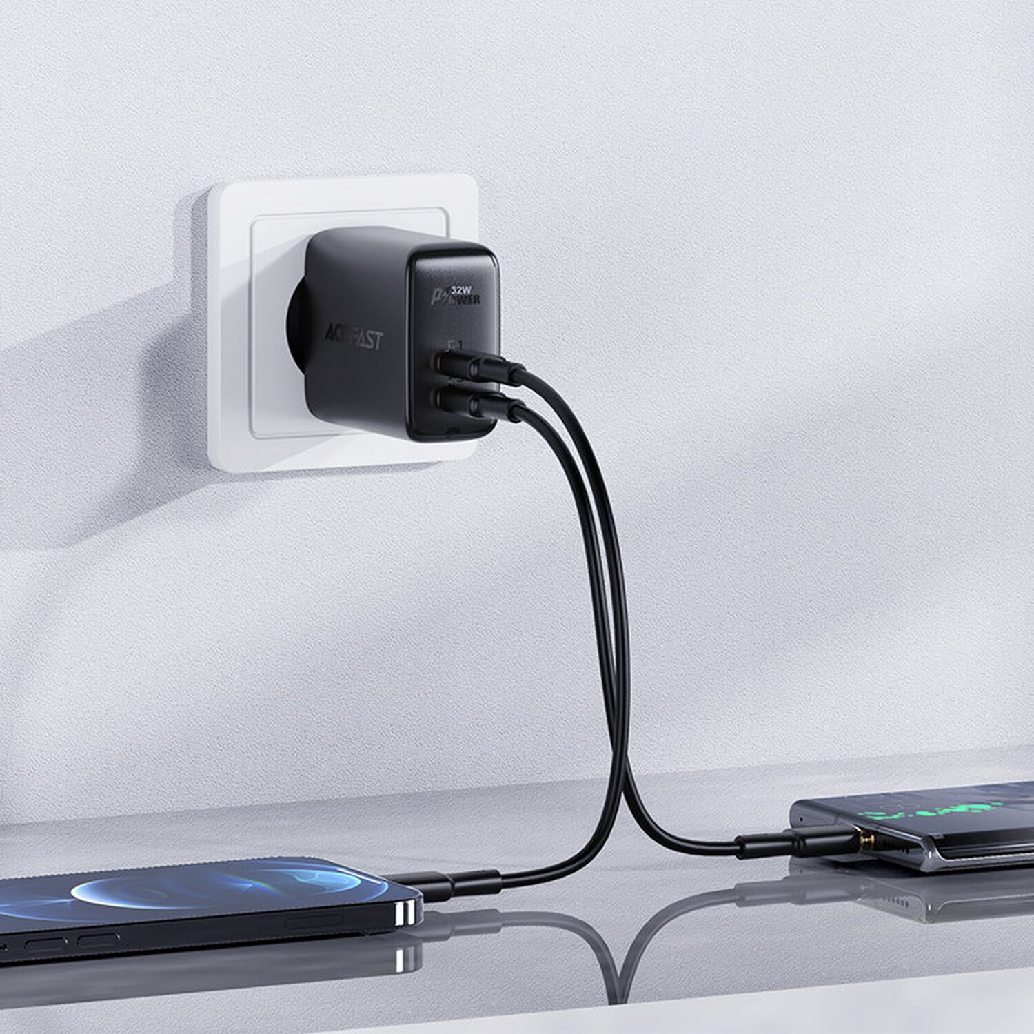 Ein schwarzes AC Fast-Ladegerät, das in eine Steckdose gesteckt wird, mit zwei über Kabel angeschlossenen Telefonen.