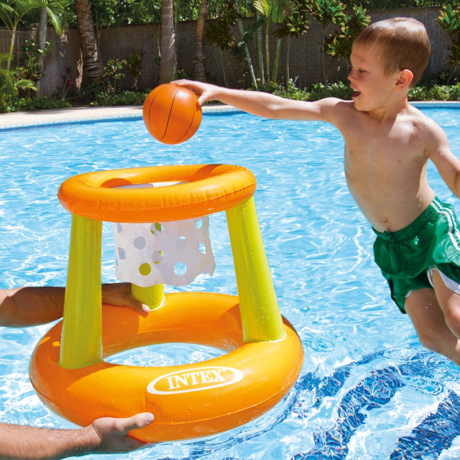 Ein Junge wirft einen Basketball in Richtung eines schwimmenden orange-gelben Basketballkorbs in einem Pool.