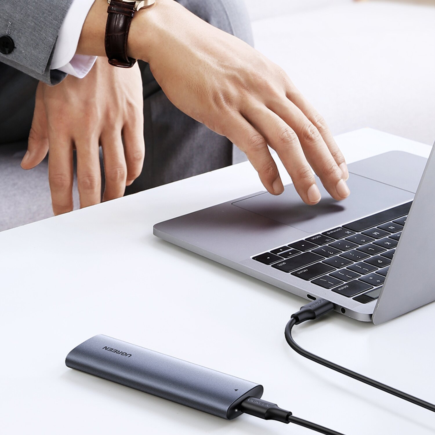 Person, die einen Laptop verwendet, der an eine graue externe Festplatte auf einem weißen Schreibtisch angeschlossen ist.