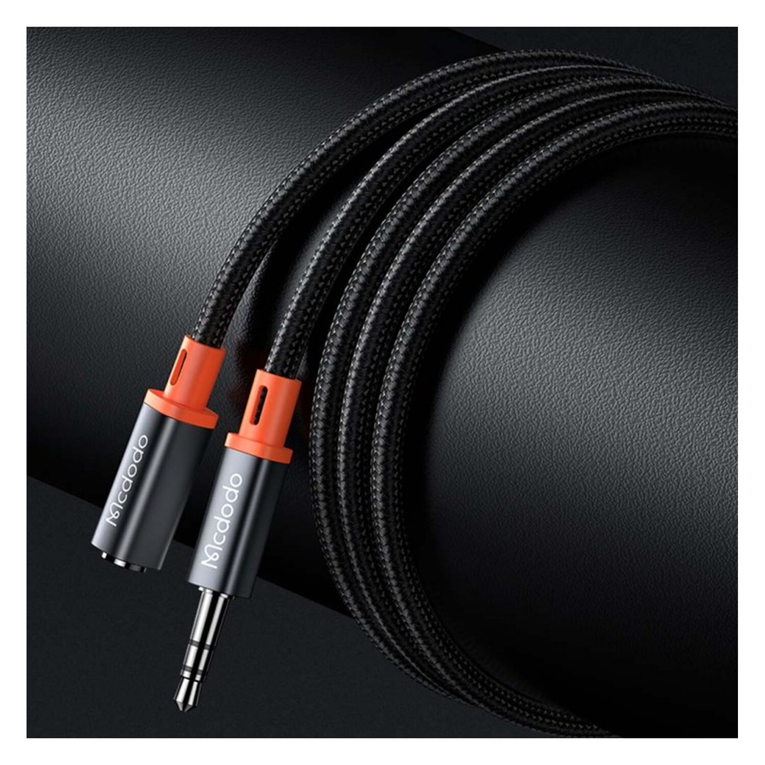 Schwarzes Audiokabel mit orangefarbenen Details. Zwei Anschlüsse. Schwarzer Hintergrund. Das Kabel ist gewickelt.