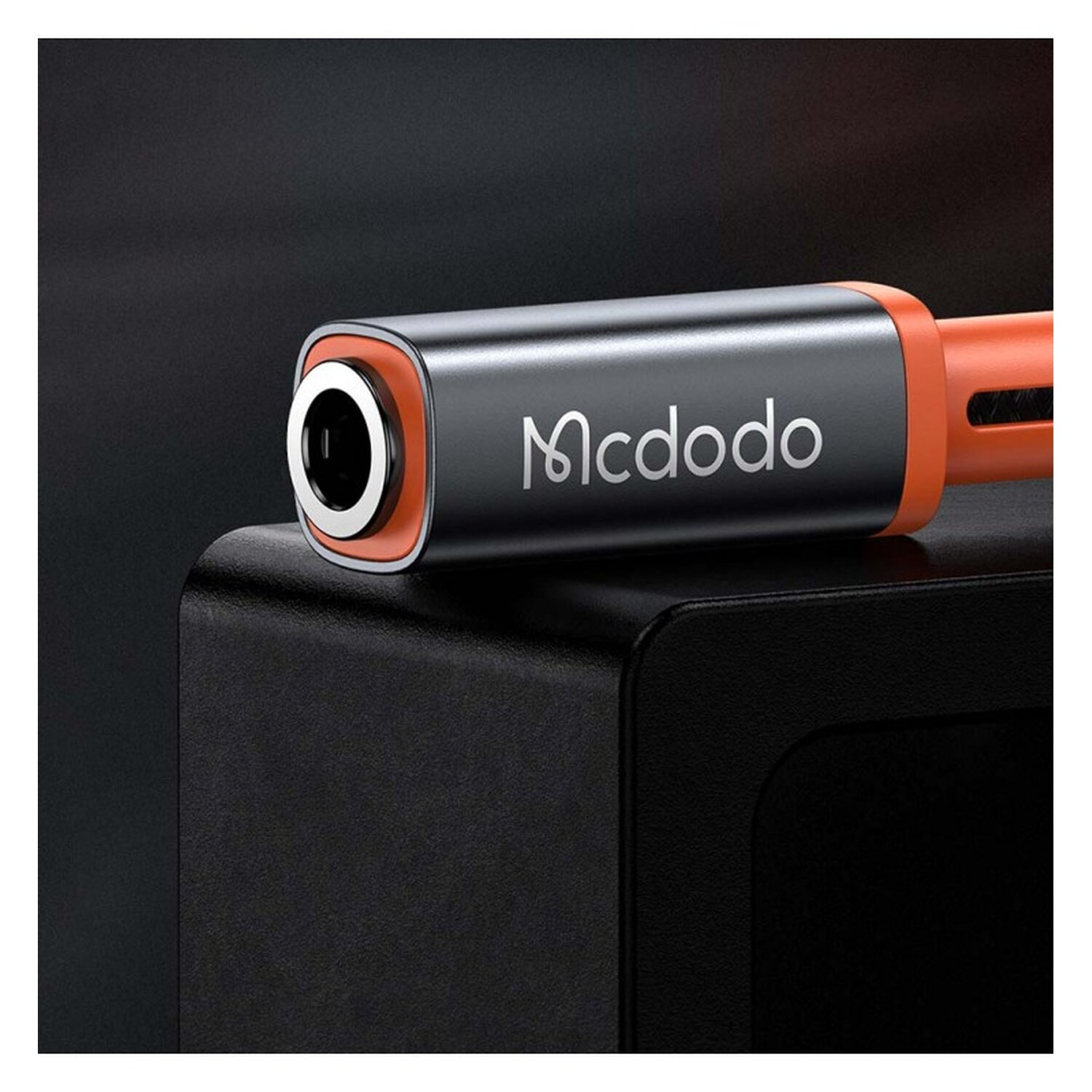 Nahaufnahme eines schwarzen und orangefarbenen Mcdodo-Audioanschlusses auf einer schwarzen Oberfläche.