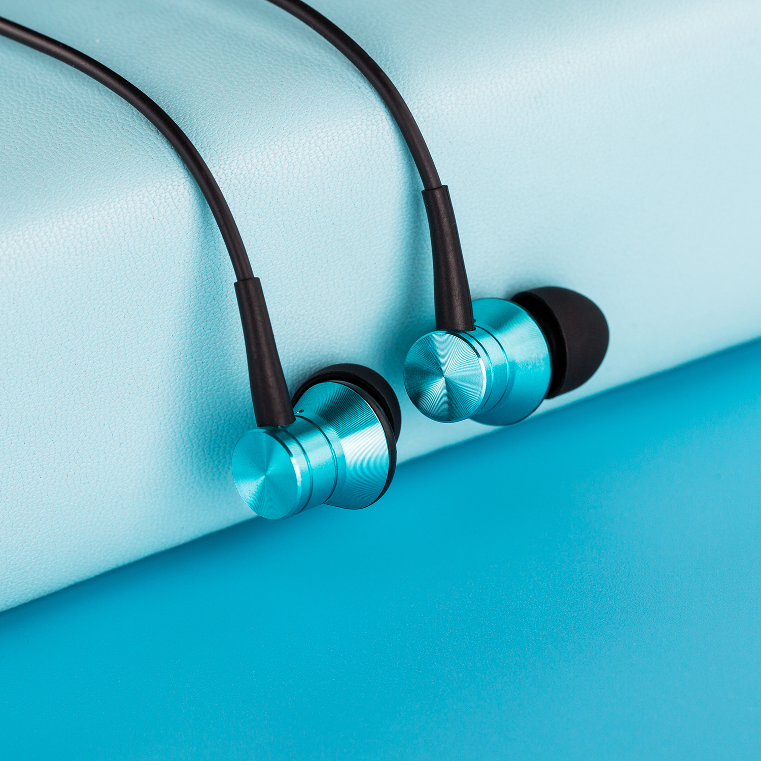 Auricolari con finitura metallica verde acqua, punte in gomma nere e cavo nero su superficie blu e verde acqua.