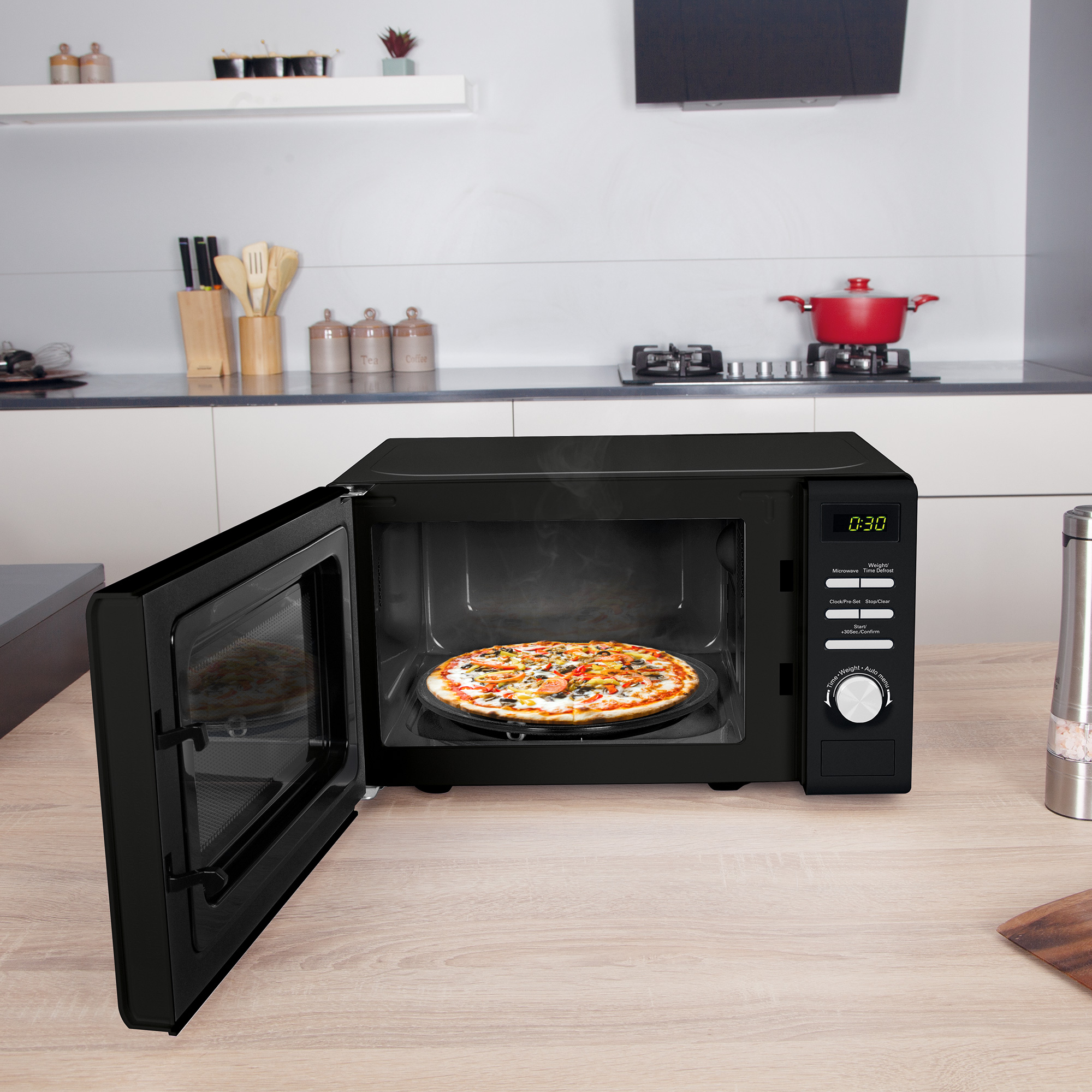 Eine schwarze Mikrowelle mit offener Tür. Eine Pizza befindet sich auf einem runden Tablett im Inneren.