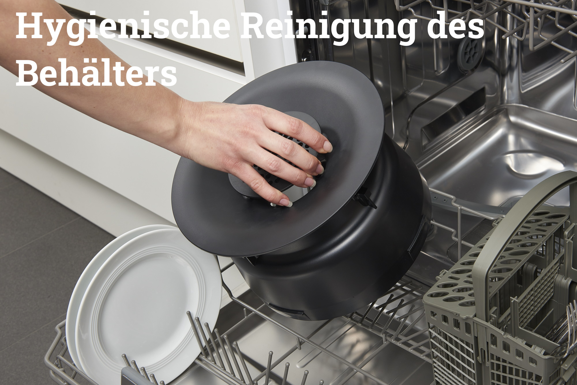 Eine Hand legt einen schwarzen Behälter in eine Spülmaschine, Teller und Gestell sind sichtbar.