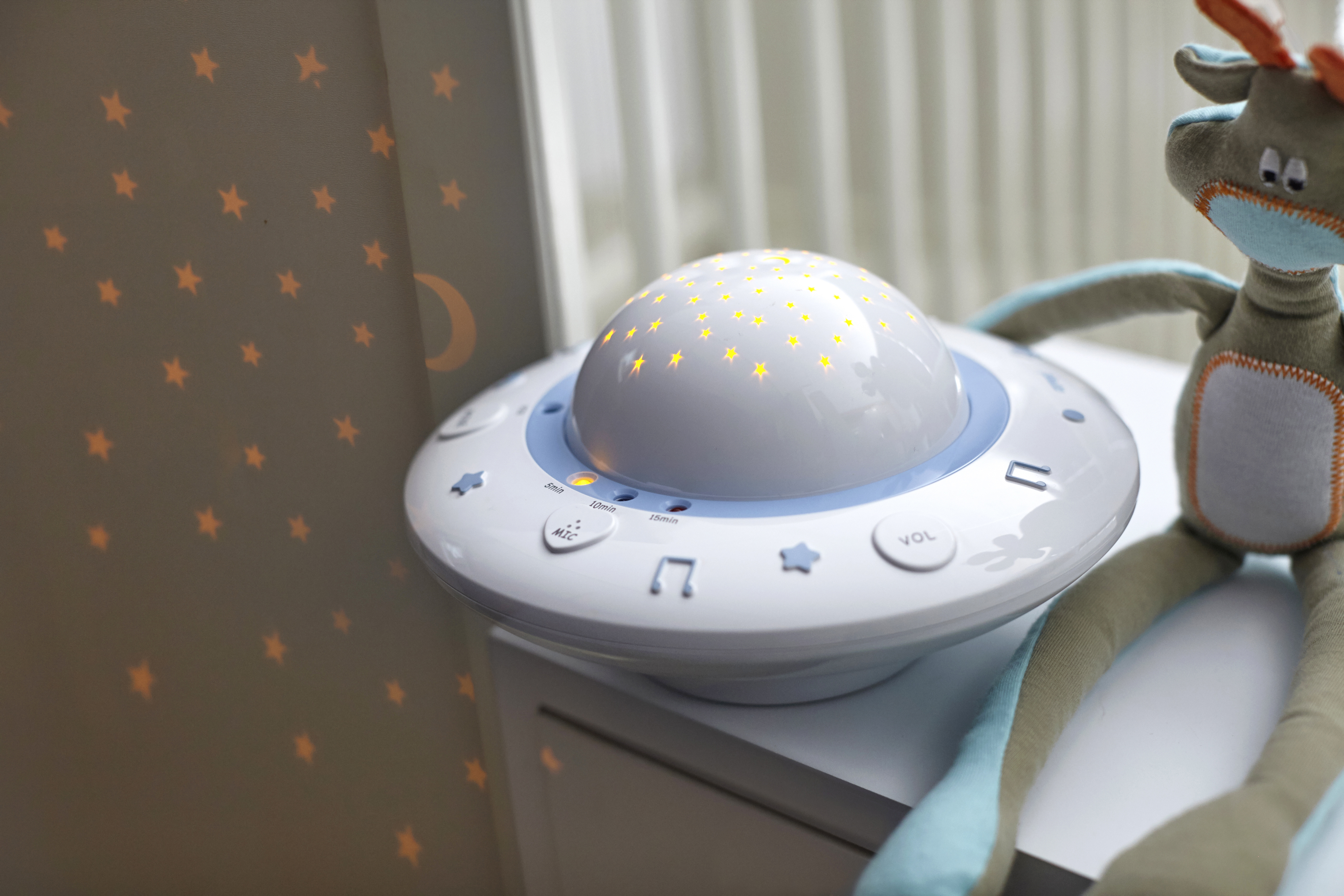 Biały projektor lampki nocnej z projekcjami gwiazd na ścianie i zabawką.