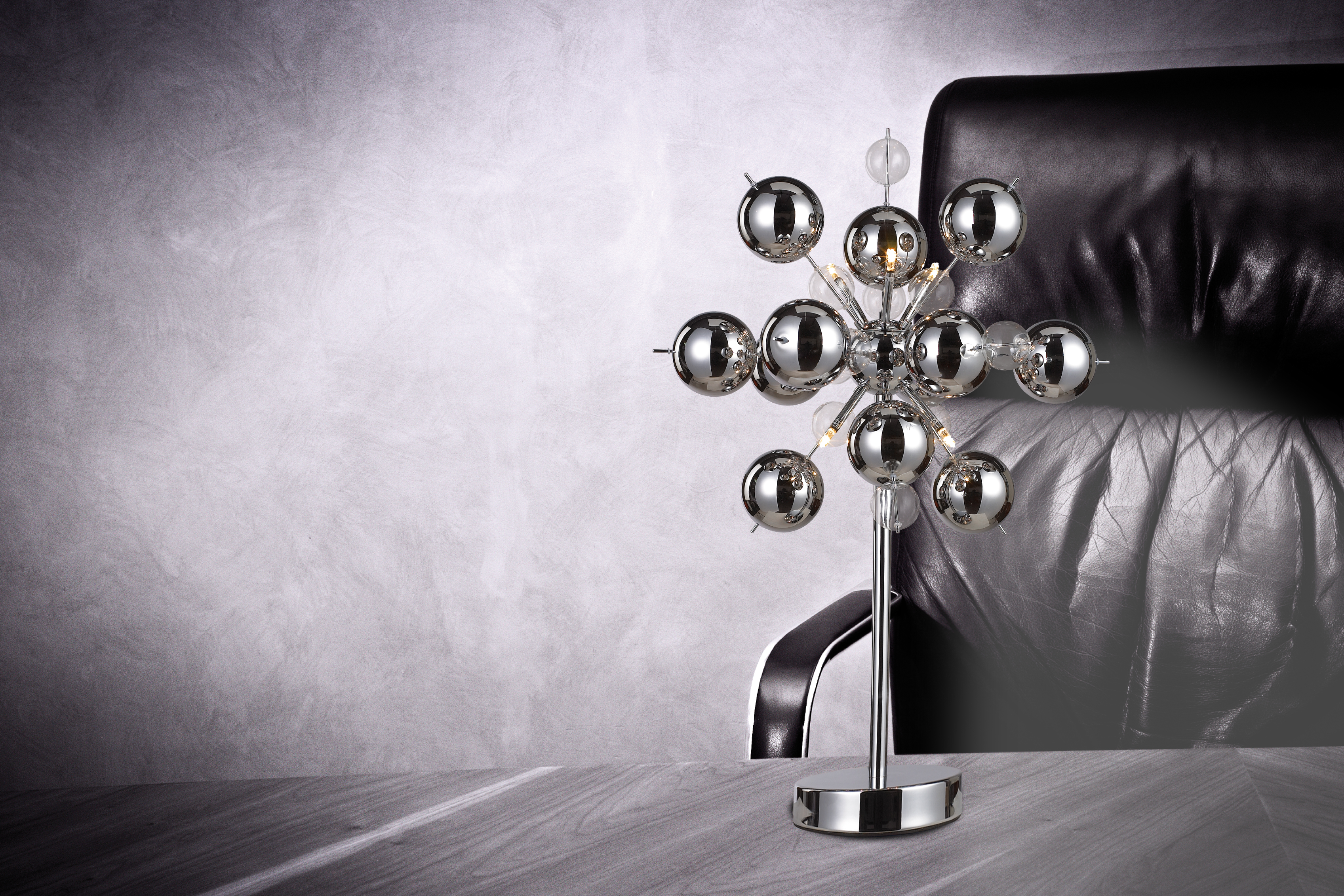 Chrom- und silberfarbene Sputnik-Lampe auf einem Holztisch. Im Hintergrund ein schwarzer Lederstuhl.