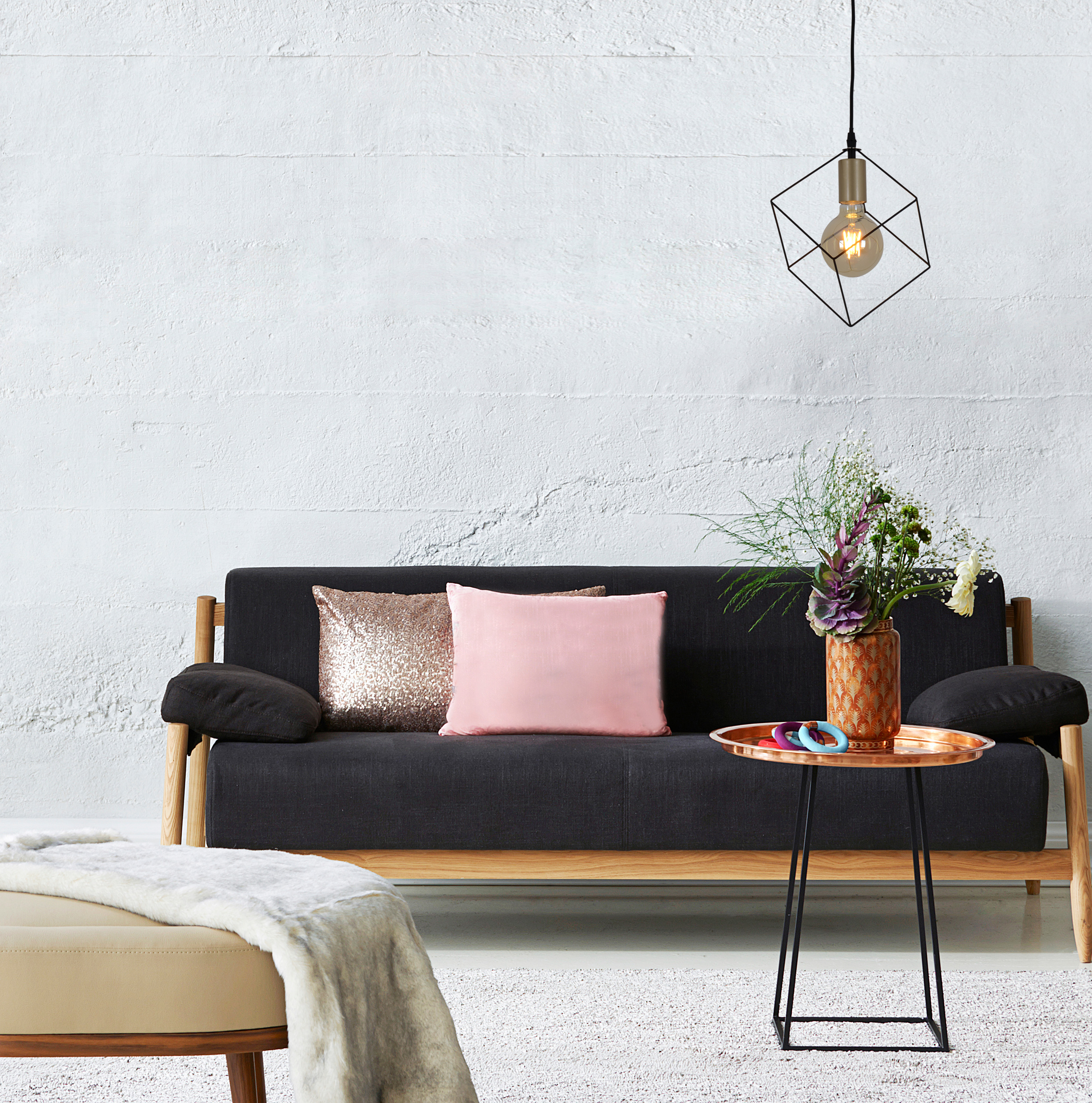 Wohnzimmerszene mit Sofa, Kissen, Beistelltisch und Pendelleuchte.