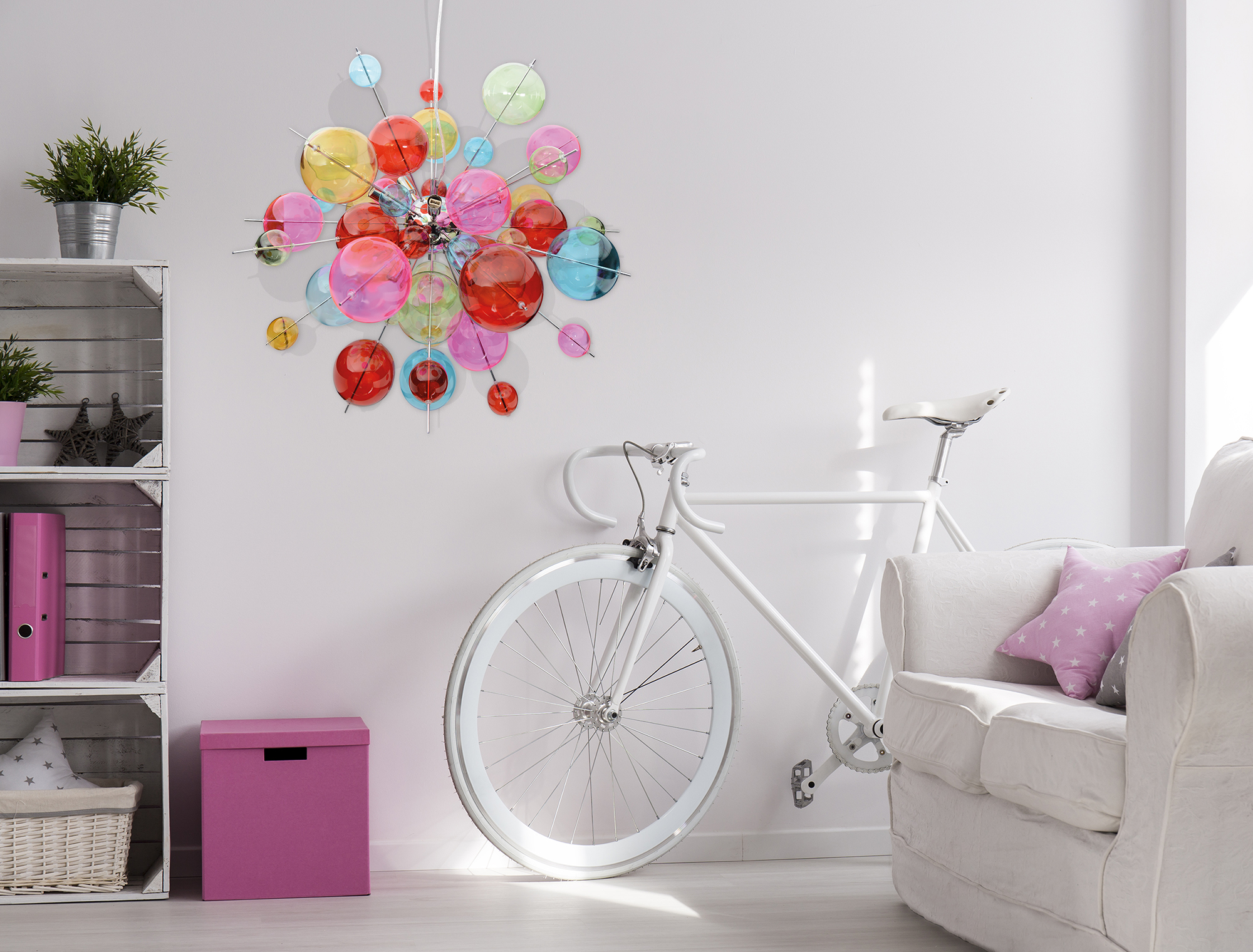 Zimmer mit weißem Fahrrad, buntem Kronleuchter und weißen Möbeln.