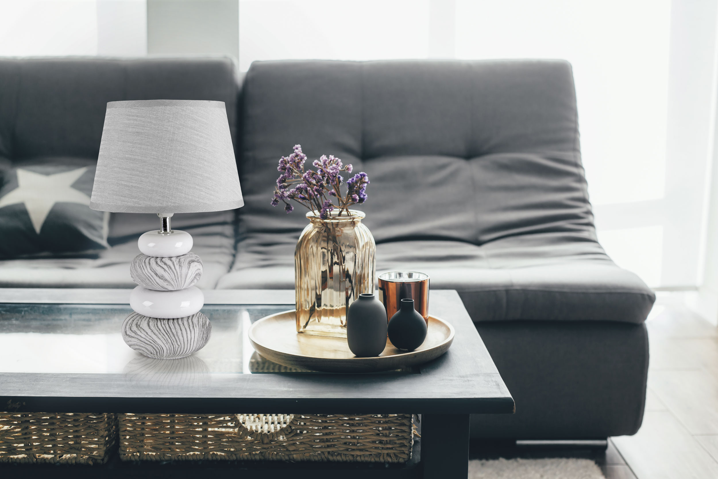 Lampe, Vase mit Blumen und Deko auf einem Tisch vor einem grauen Sofa.