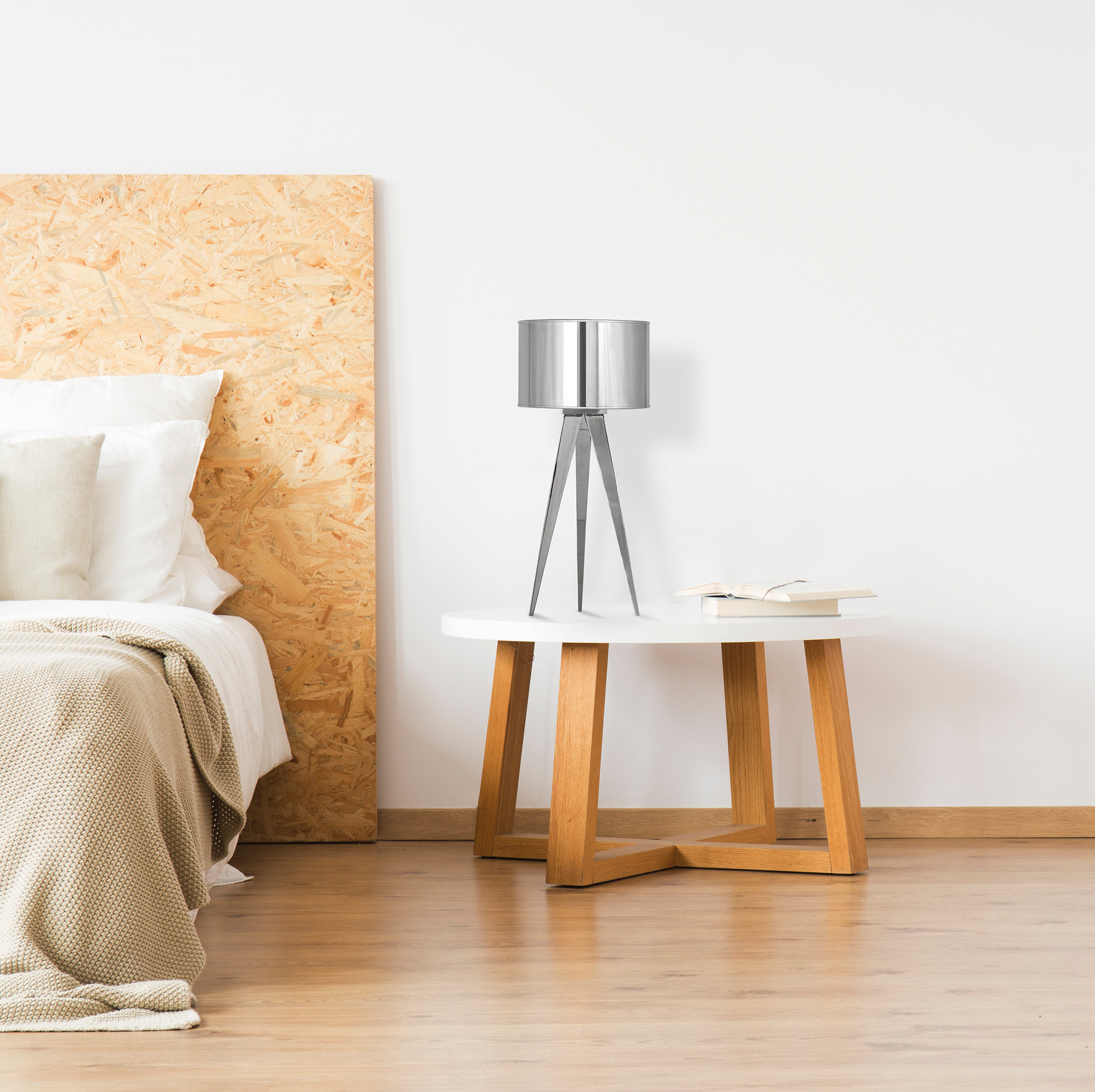 Eine silberne Lampe auf einem weißen Tisch, mit einem Bett im Hintergrund.