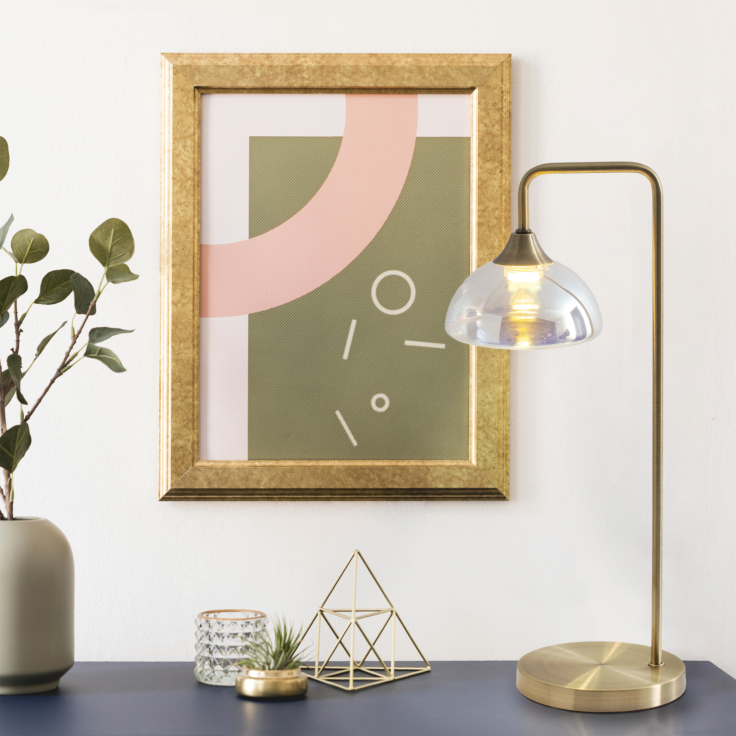Goldgerahmte Kunst, goldene Lampe mit Glasschirm, grüne Vase mit Pflanze und Deko auf blauem Tisch.