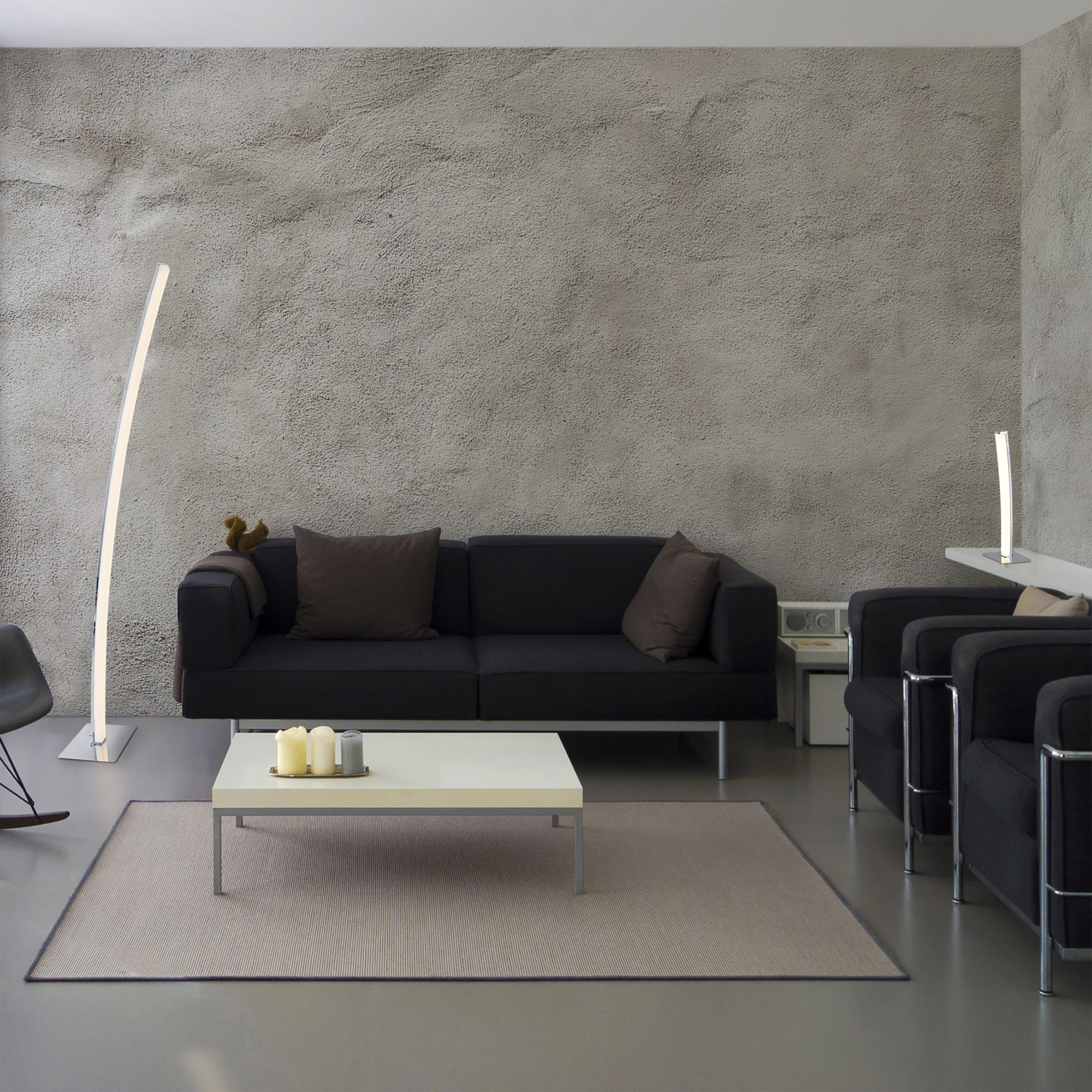 Modernes Wohnzimmer mit schwarzem Sofa, weißem Tisch und hoher, geschwungener Stehlampe.