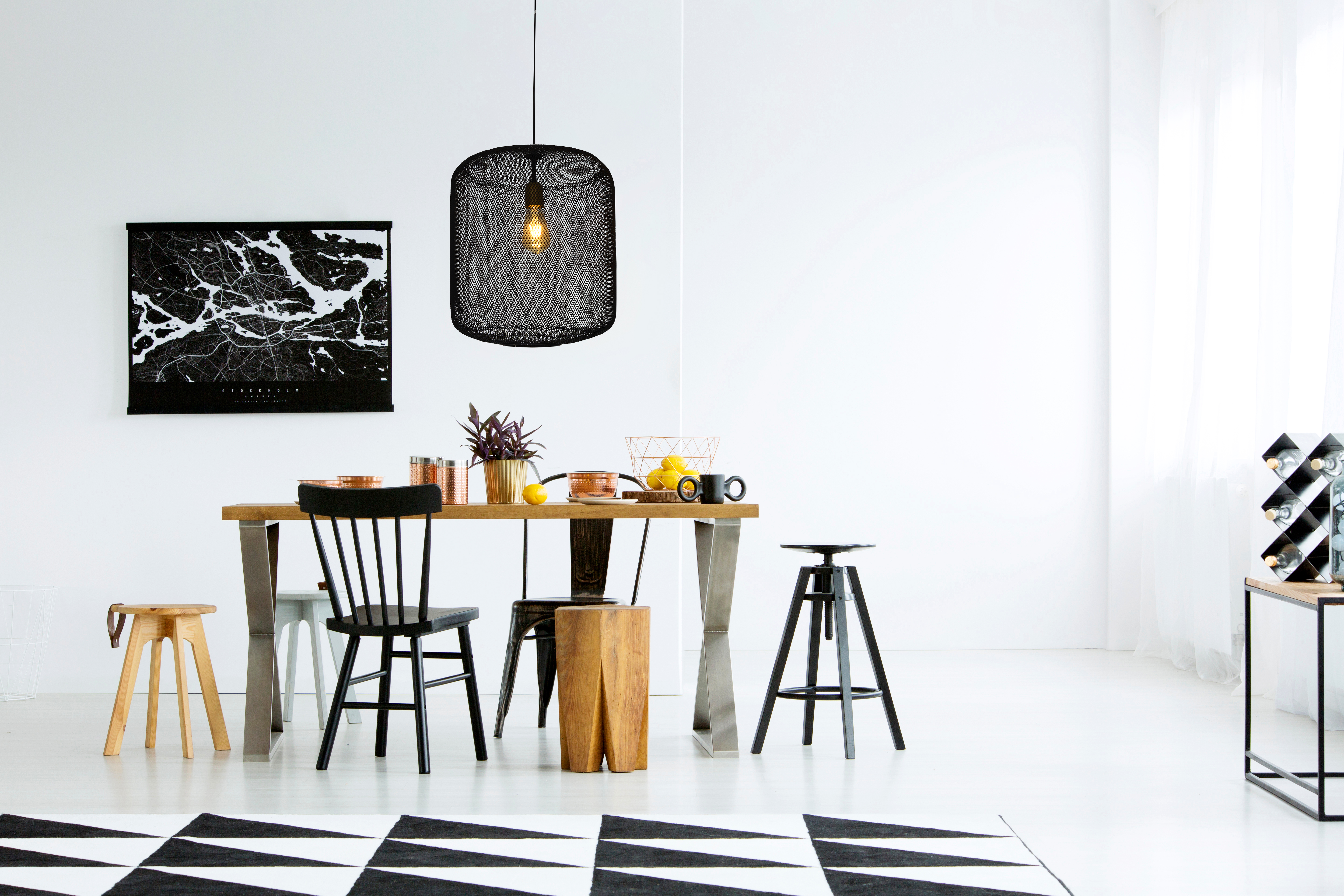 Esszimmer mit Holztisch, schwarzen Stühlen, Karte und Pendelleuchte. Weiße Wand.