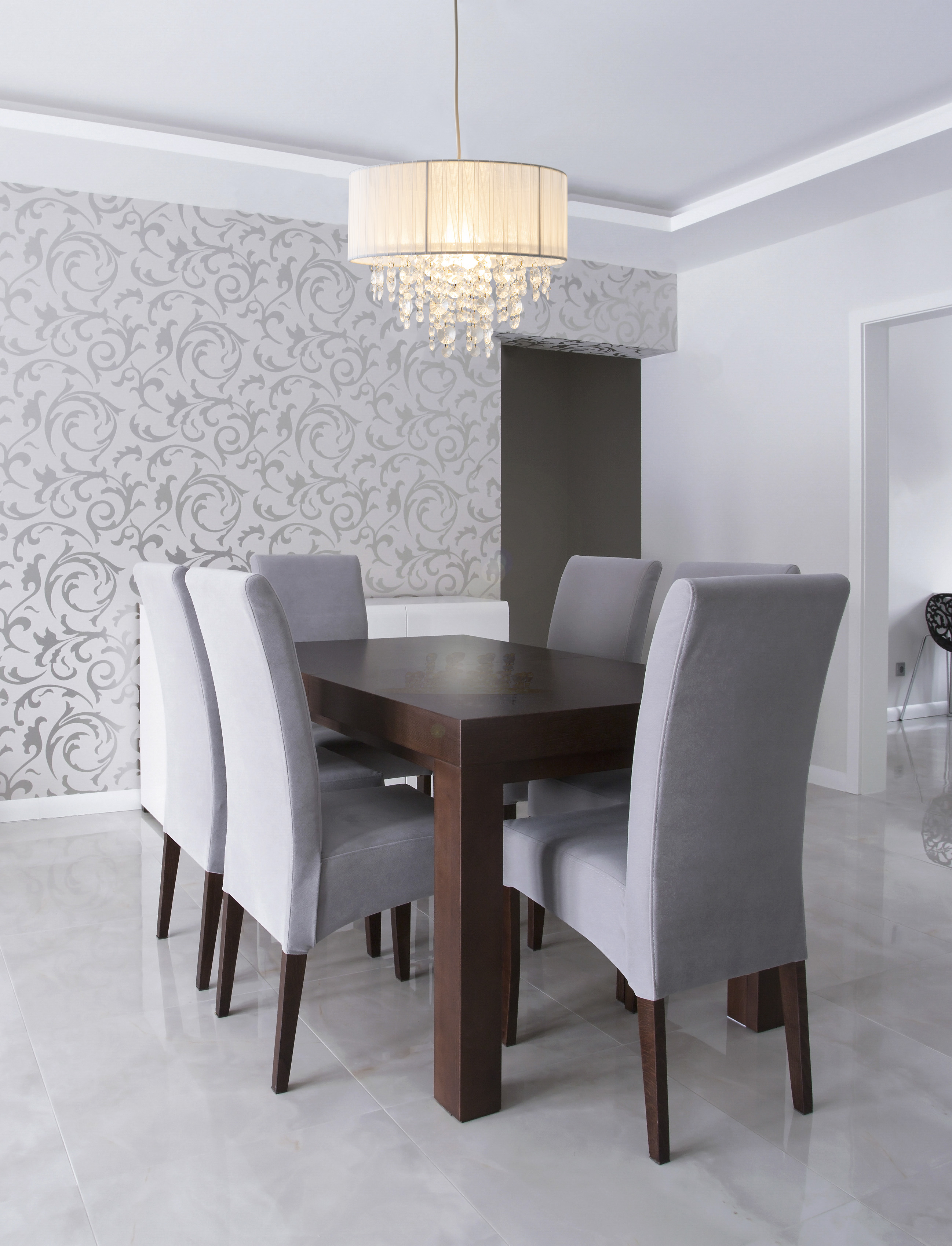 Esszimmer mit Tisch, sechs Stühlen und Kronleuchter. Die Tapete hat ein Blumenmuster.