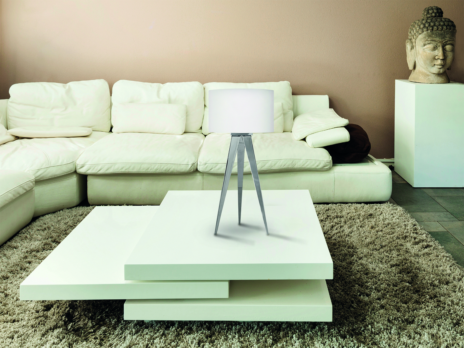 Eine Lampe mit weißem Schirm auf Stativbeinen steht auf einem weißen Tisch, mit weißem Sofa und Buddha-Statue.