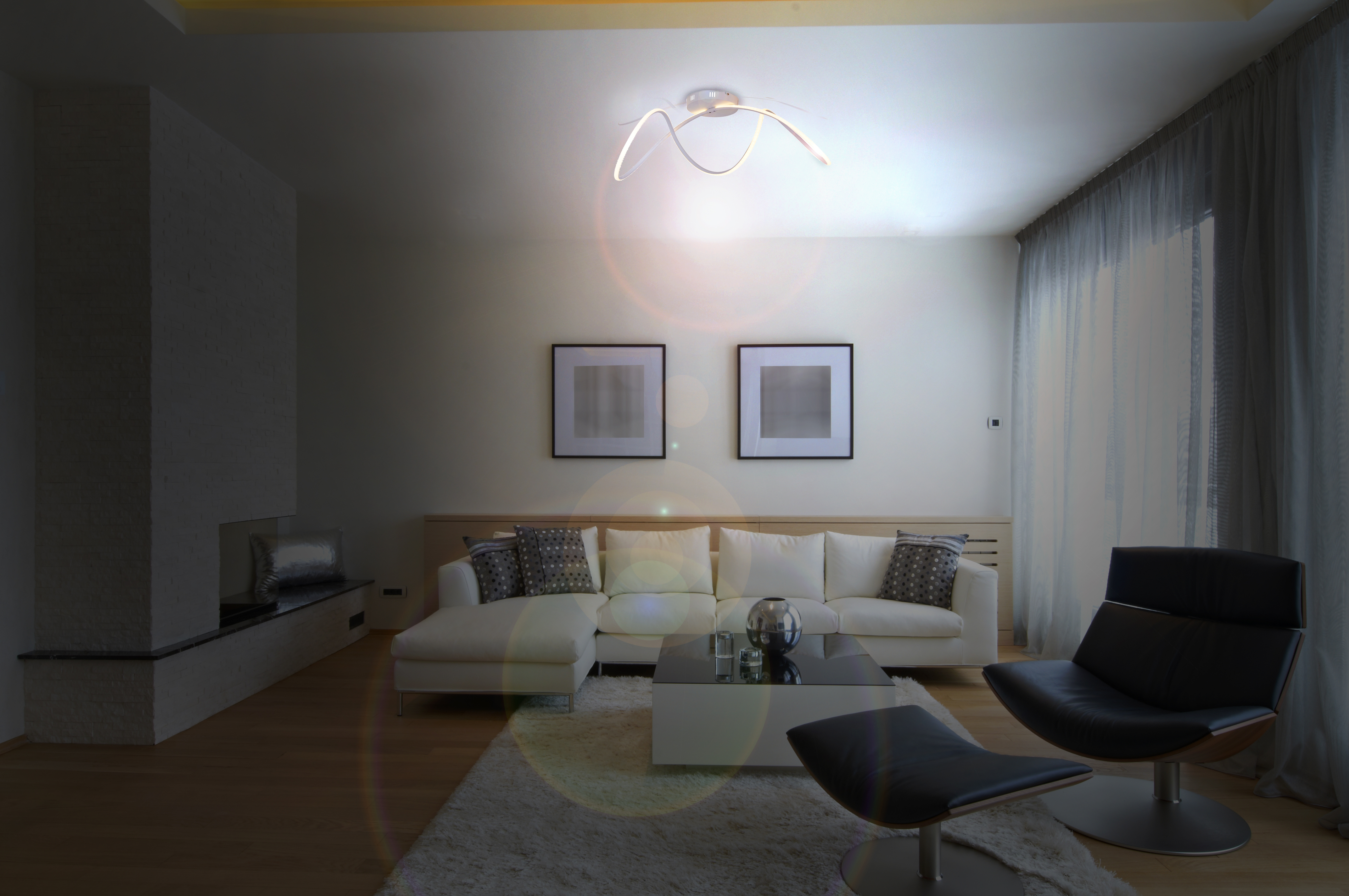 Ein modernes Wohnzimmer mit weißem Sofa, zwei Bildern und einer modernen Deckenleuchte.