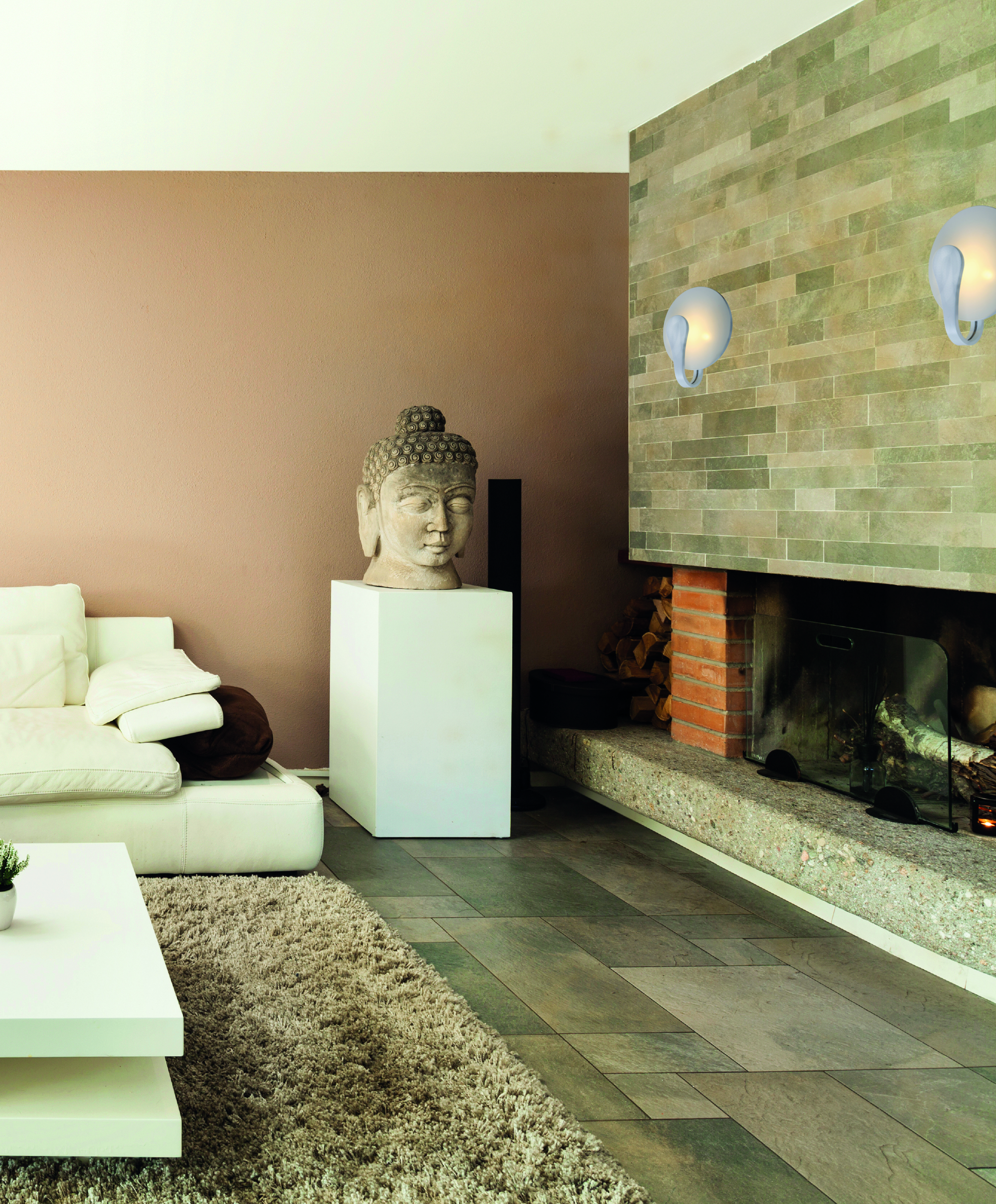 Wohnzimmer mit einem Buddha-Kopf auf einem Sockel, Kamin, Sofa und Wandleuchten.