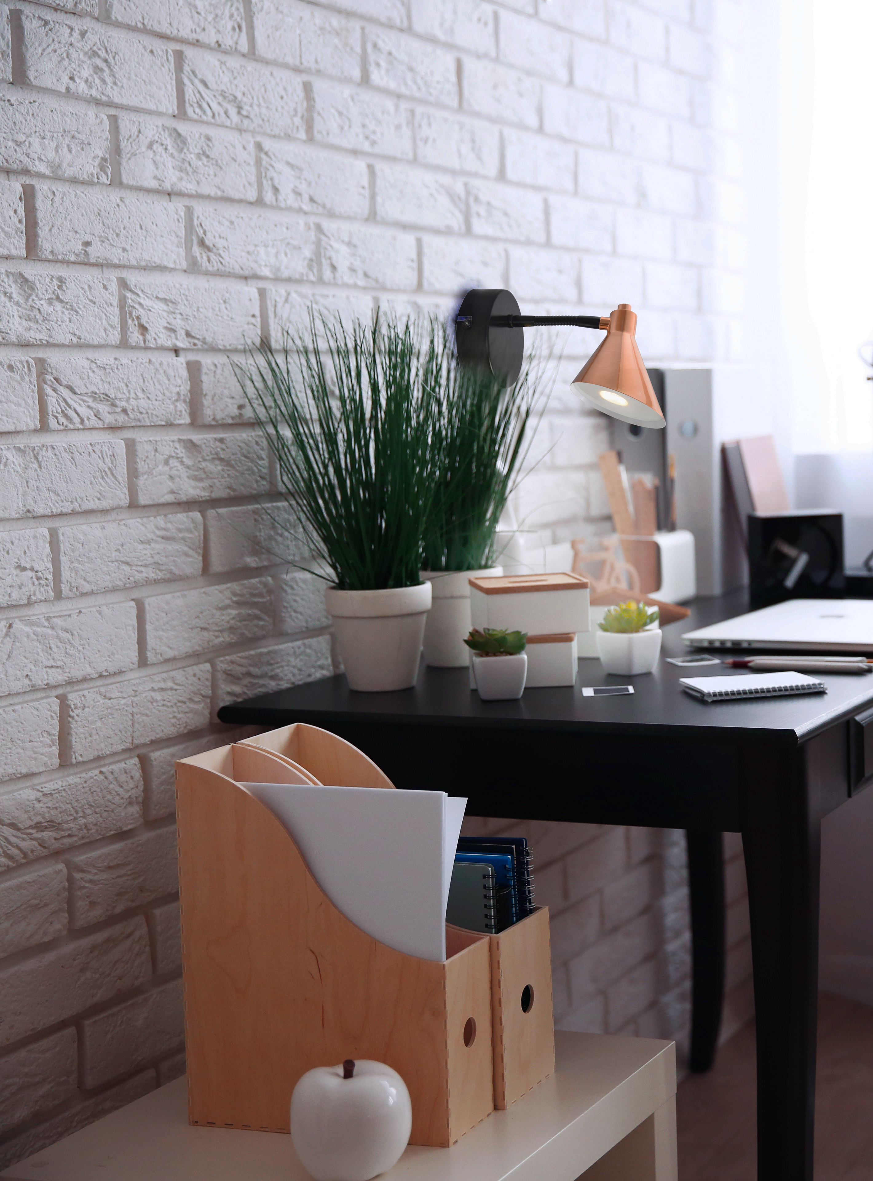 Schreibtisch mit Büromaterial, Backsteinmauer im Hintergrund.