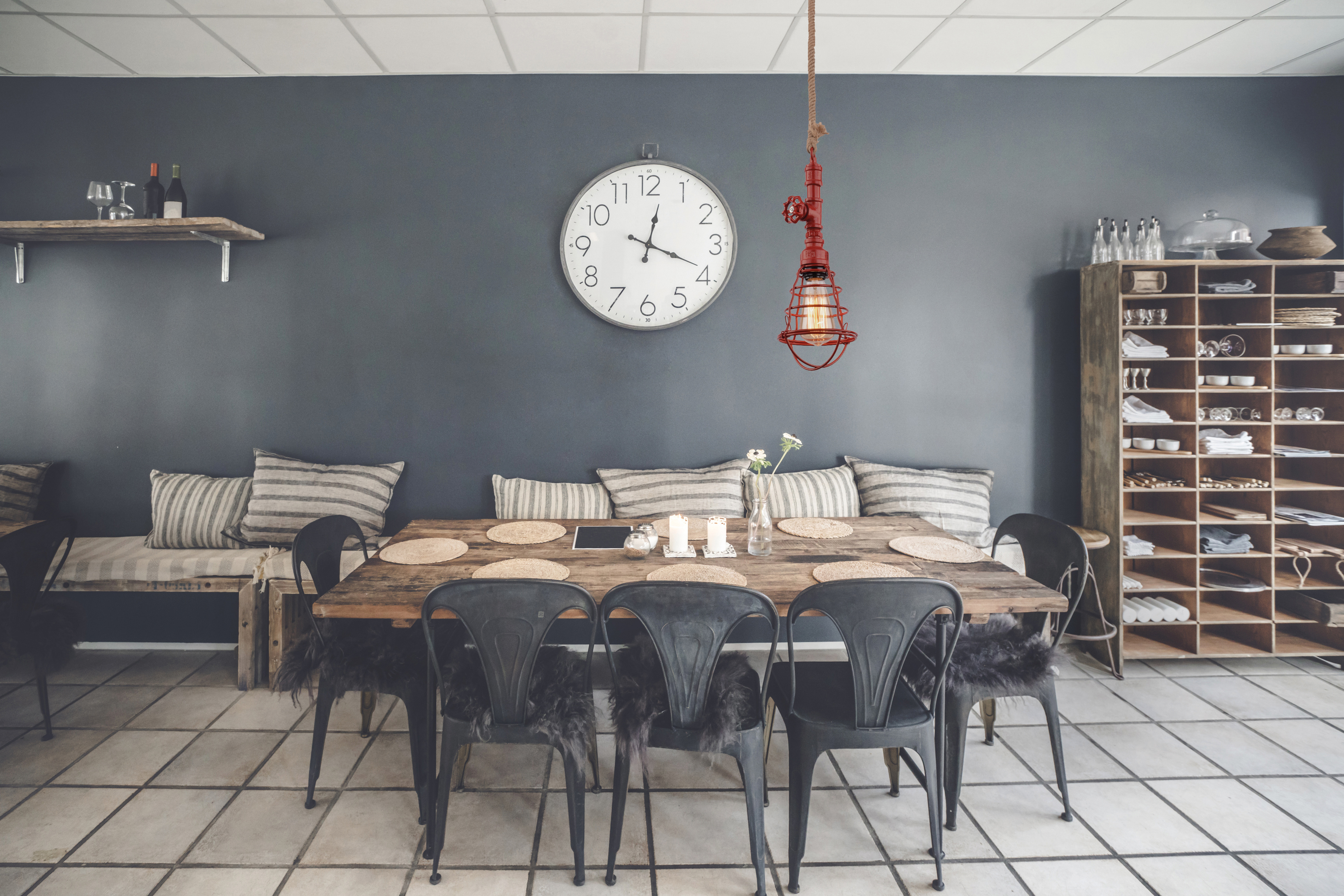 Esszimmer mit Tisch, Stühlen und einer hängenden roten Leuchte. Dunkle Wand.