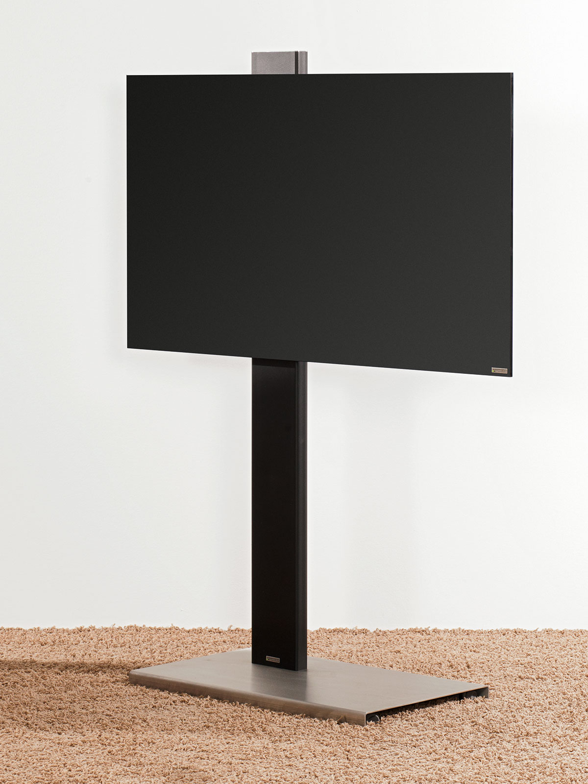 Schwarzer Fernseher auf Ständer, beiger Teppich, weiße Wand.