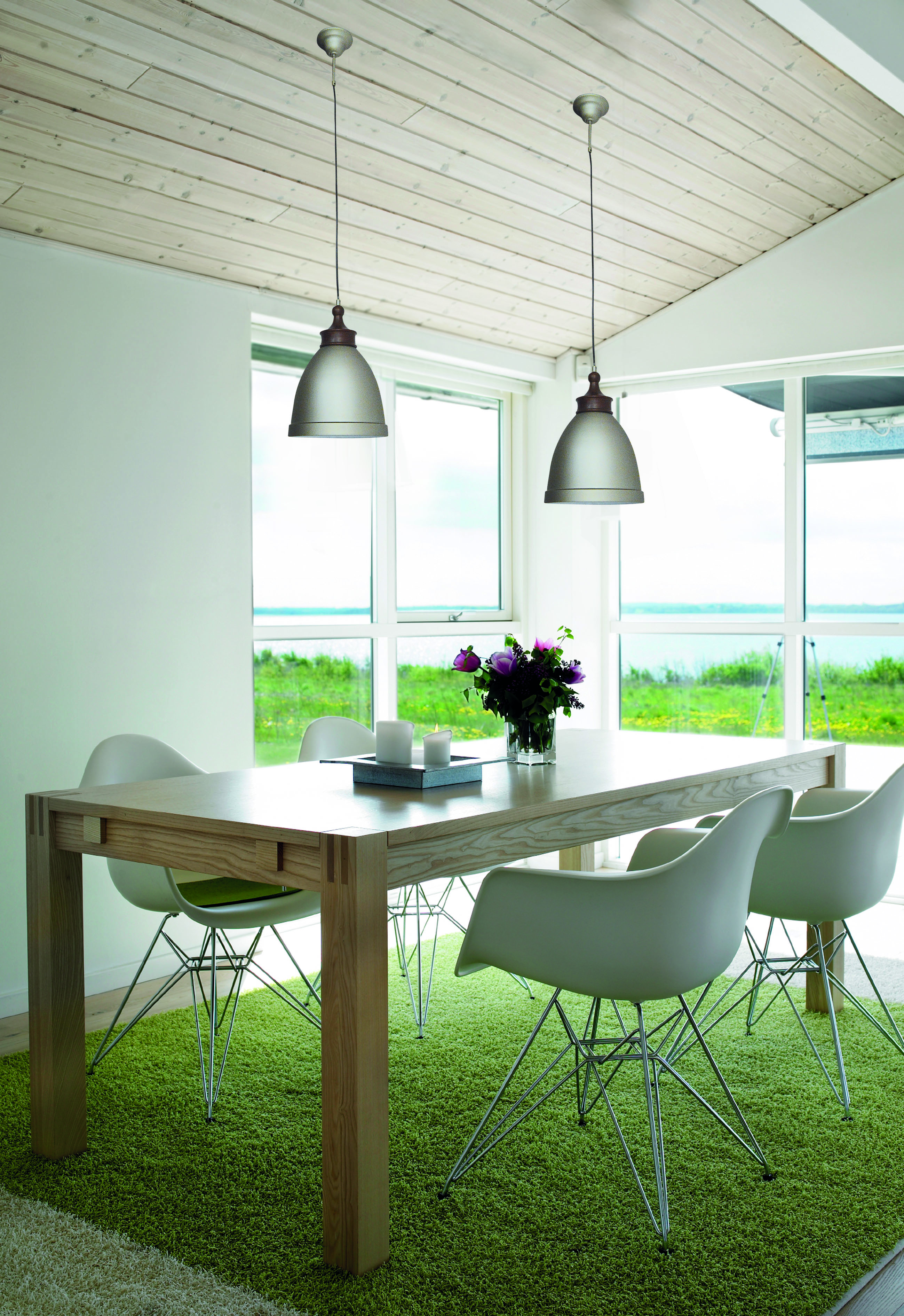 Esszimmer mit Tisch, Stühlen und Pendelleuchten über grünem Teppich.