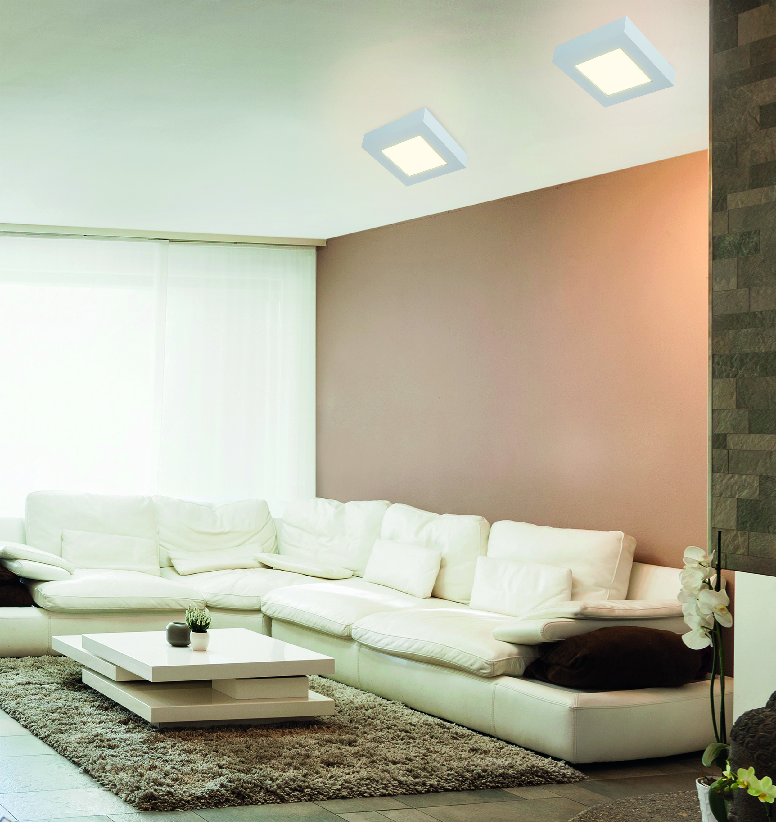 Modernes Wohnzimmer mit weißem Sofa, weißem Tisch, zwei quadratischen Deckenleuchten und hellbraunen Wänden.