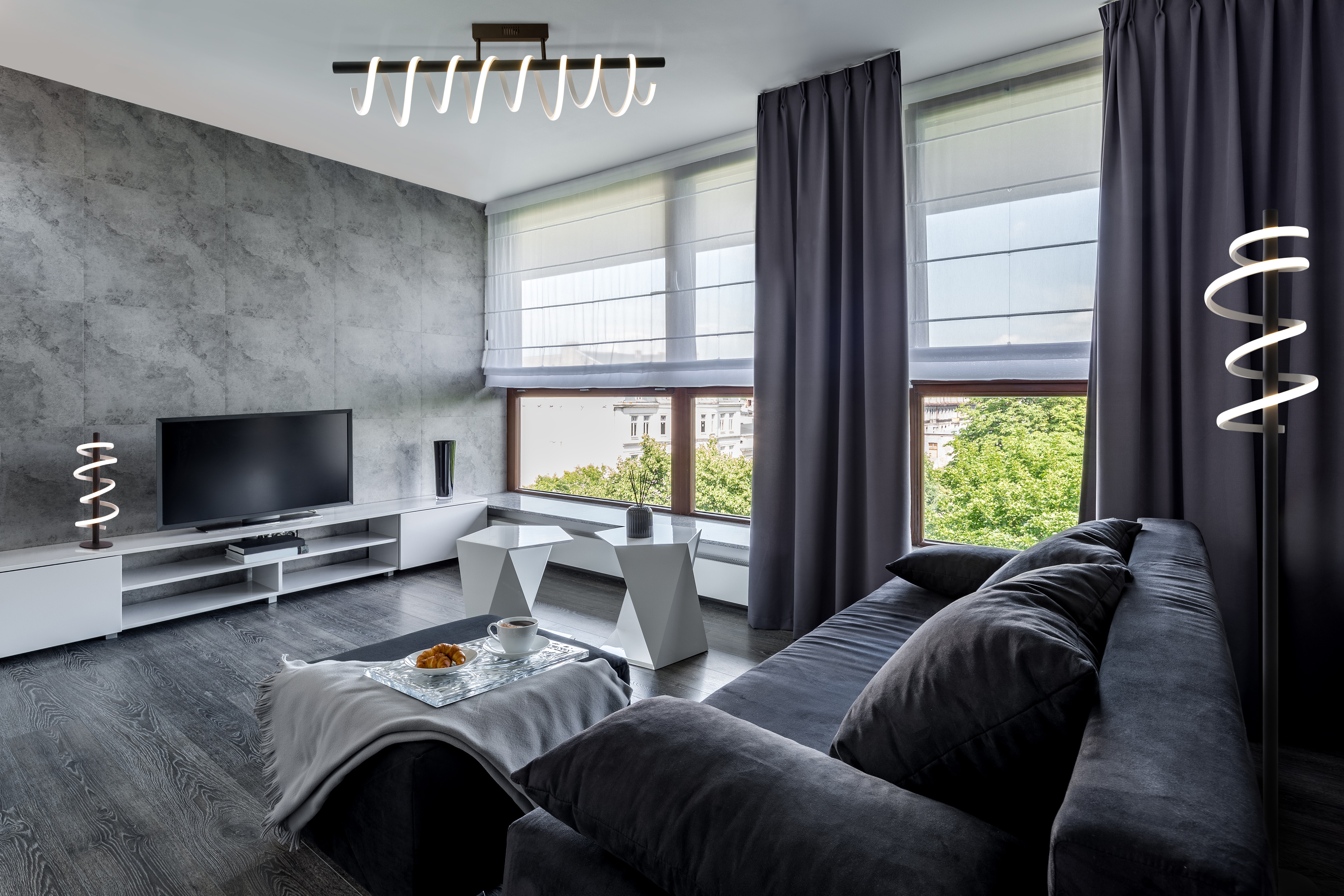 Ein modernes Wohnzimmer mit grauen Wänden, einem schwarzen Fernseher und einem dunkelgrauen Sofa.