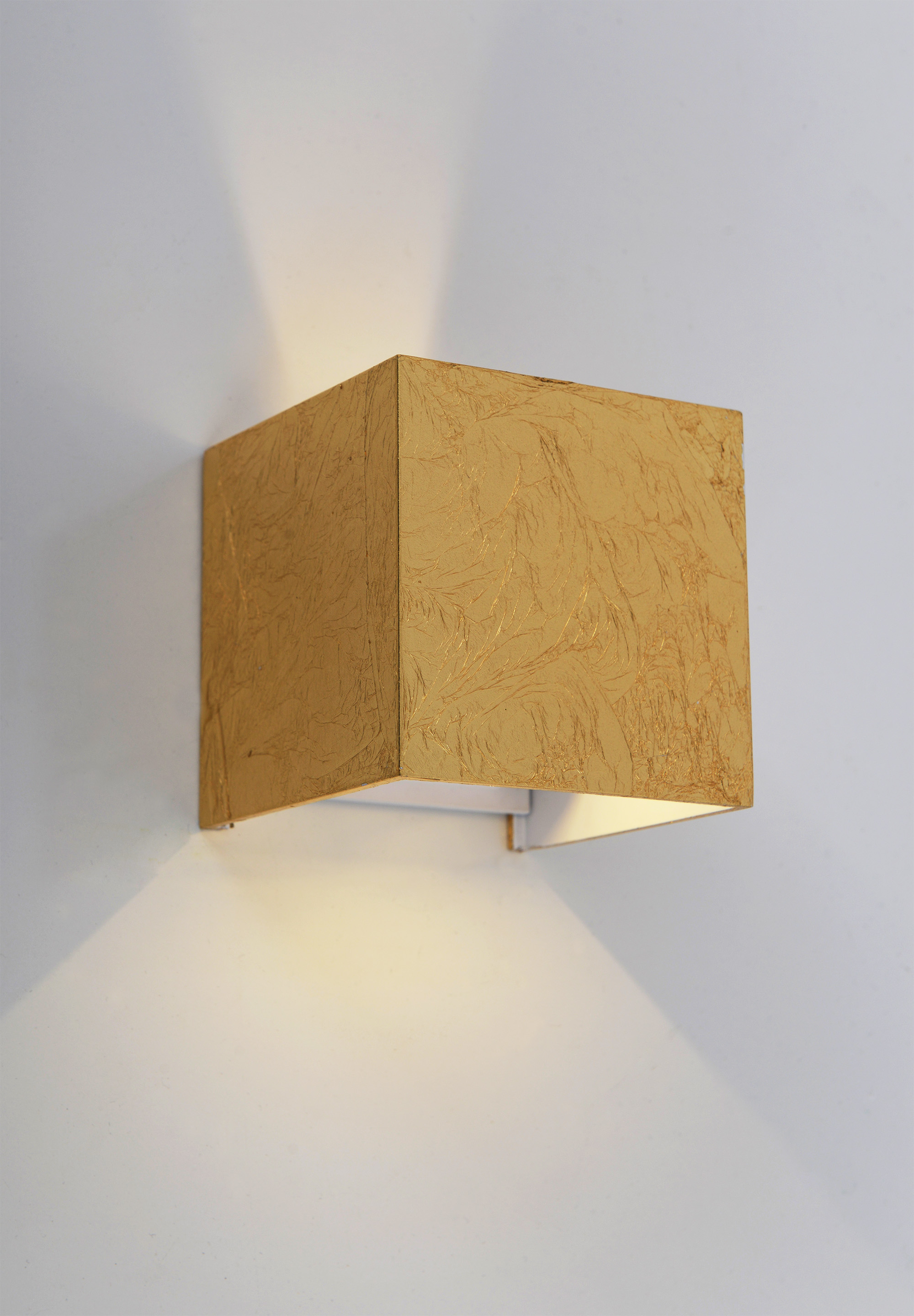Quadratische goldene Wandleuchte, die Licht nach unten wirft, an einer weißen Wand montiert.