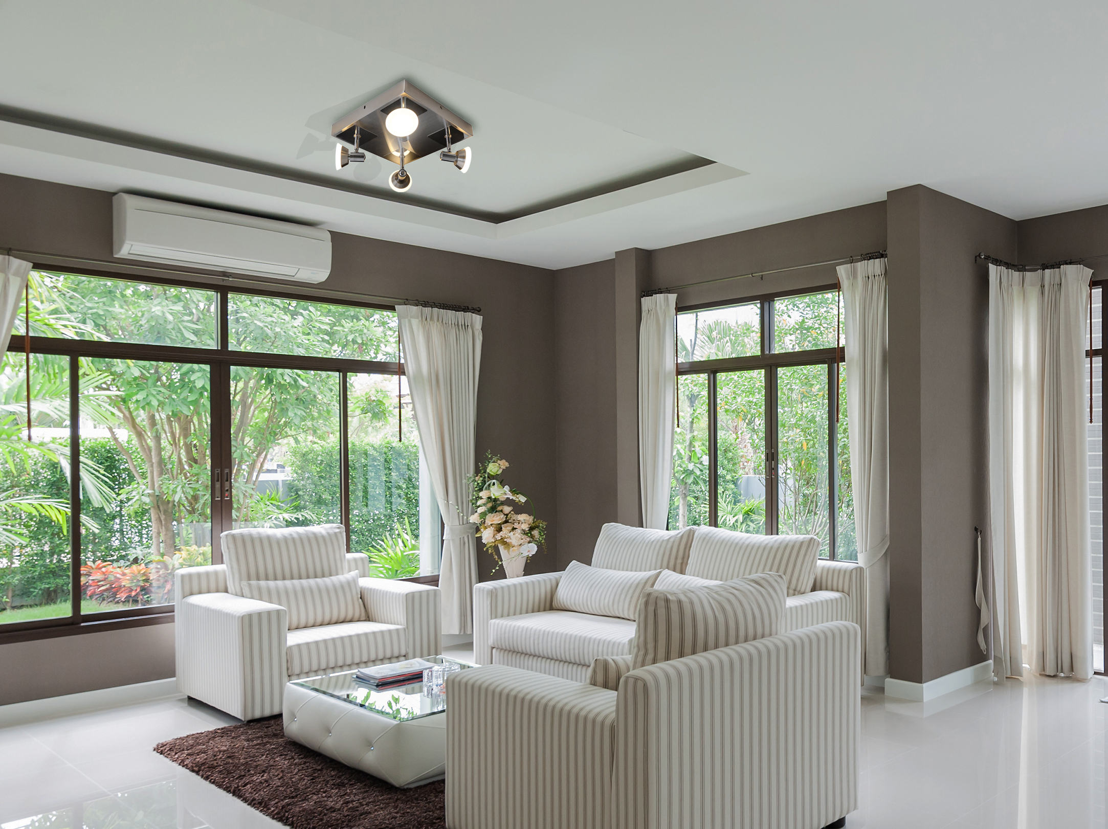 Ein Wohnzimmer mit weißen Sofas, einem Glastisch und großen Fenstern mit Blick auf einen Garten.