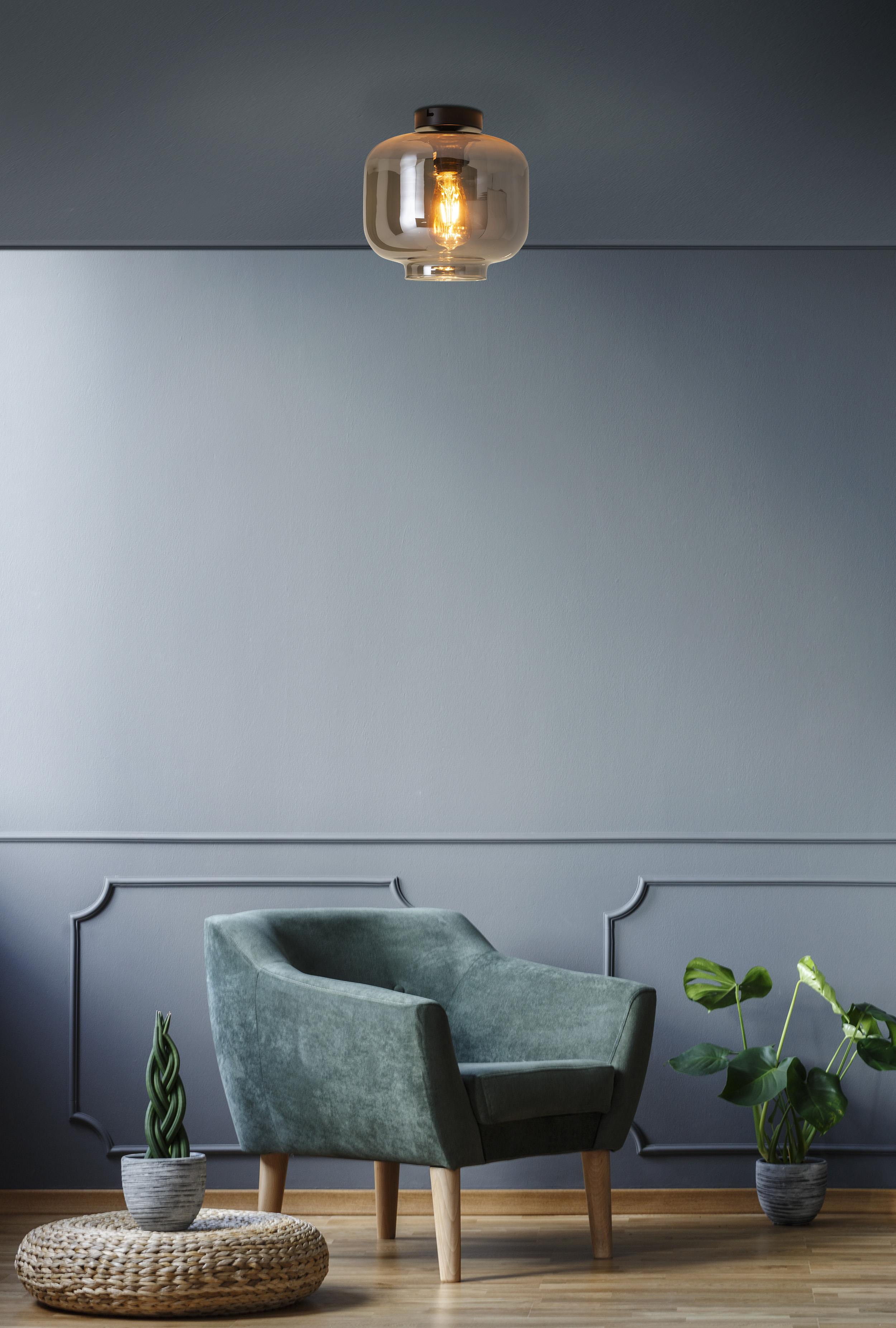 Une pièce avec un luminaire, un fauteuil vert et des plantes. Les murs sont gris.