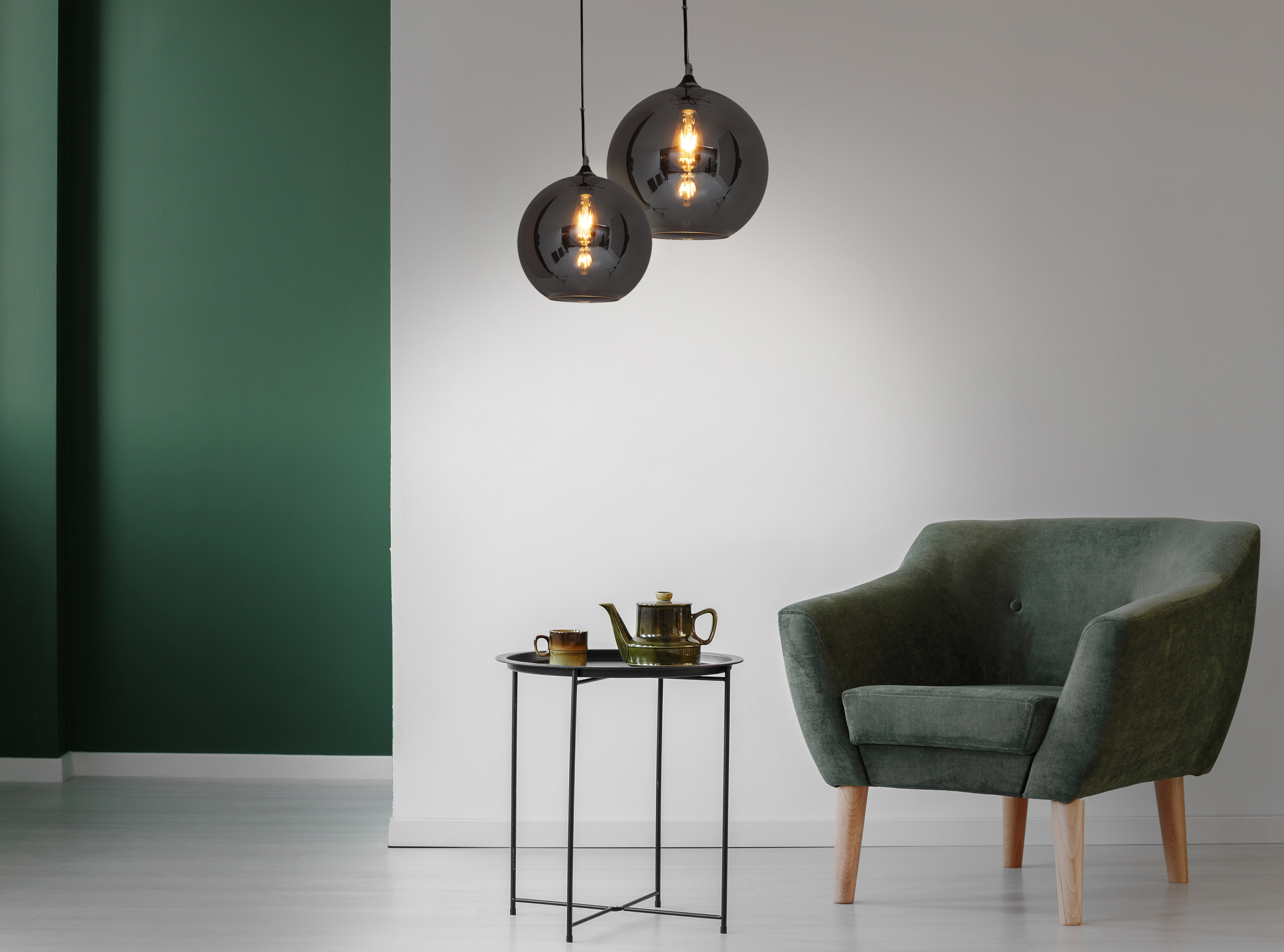 Zwei Pendelleuchten über einem Tisch mit Teeset und einem Sessel.
