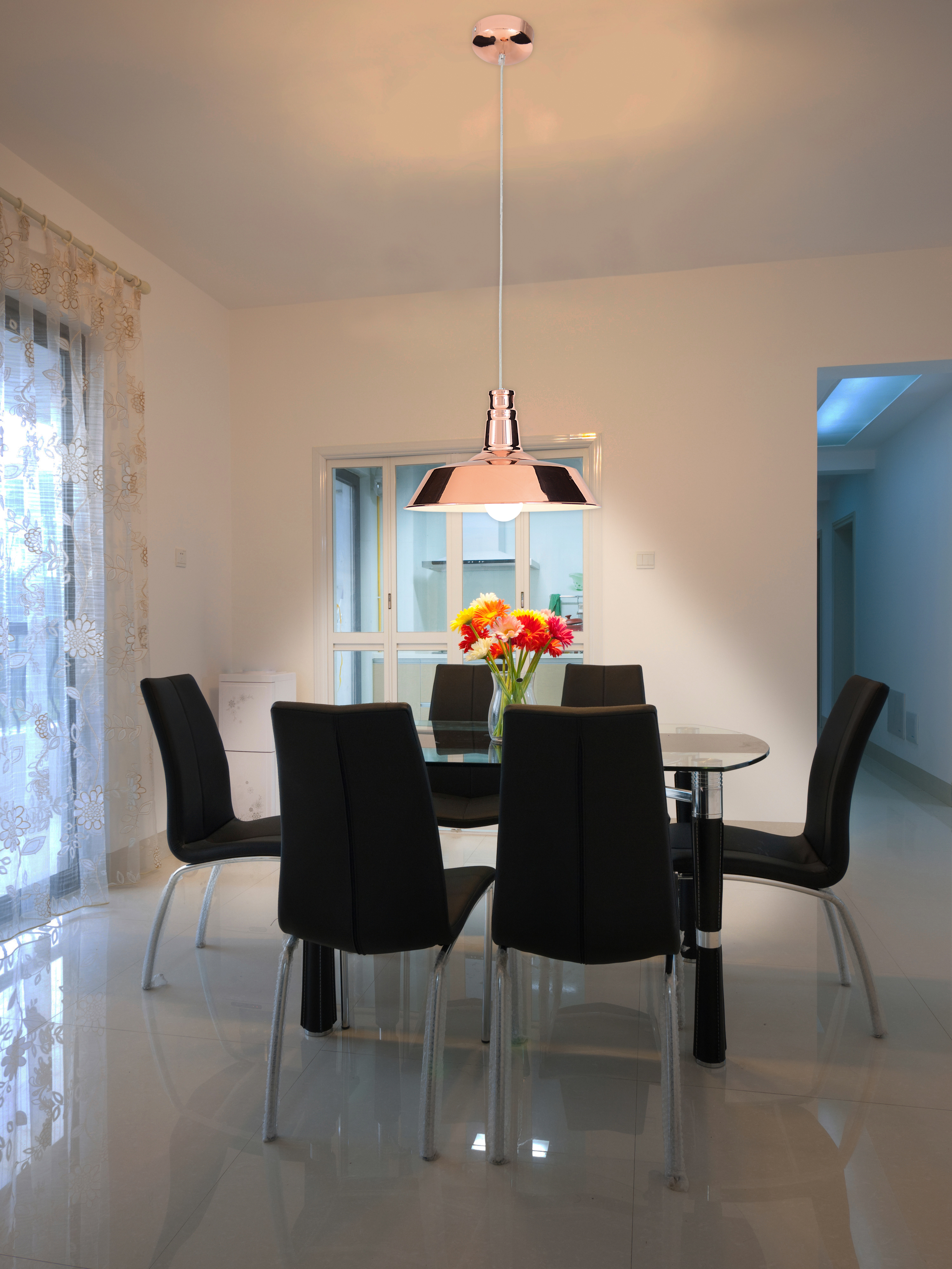 Esszimmer mit rundem Glastisch, sechs schwarzen Stühlen und einer kupferfarbenen Pendelleuchte.