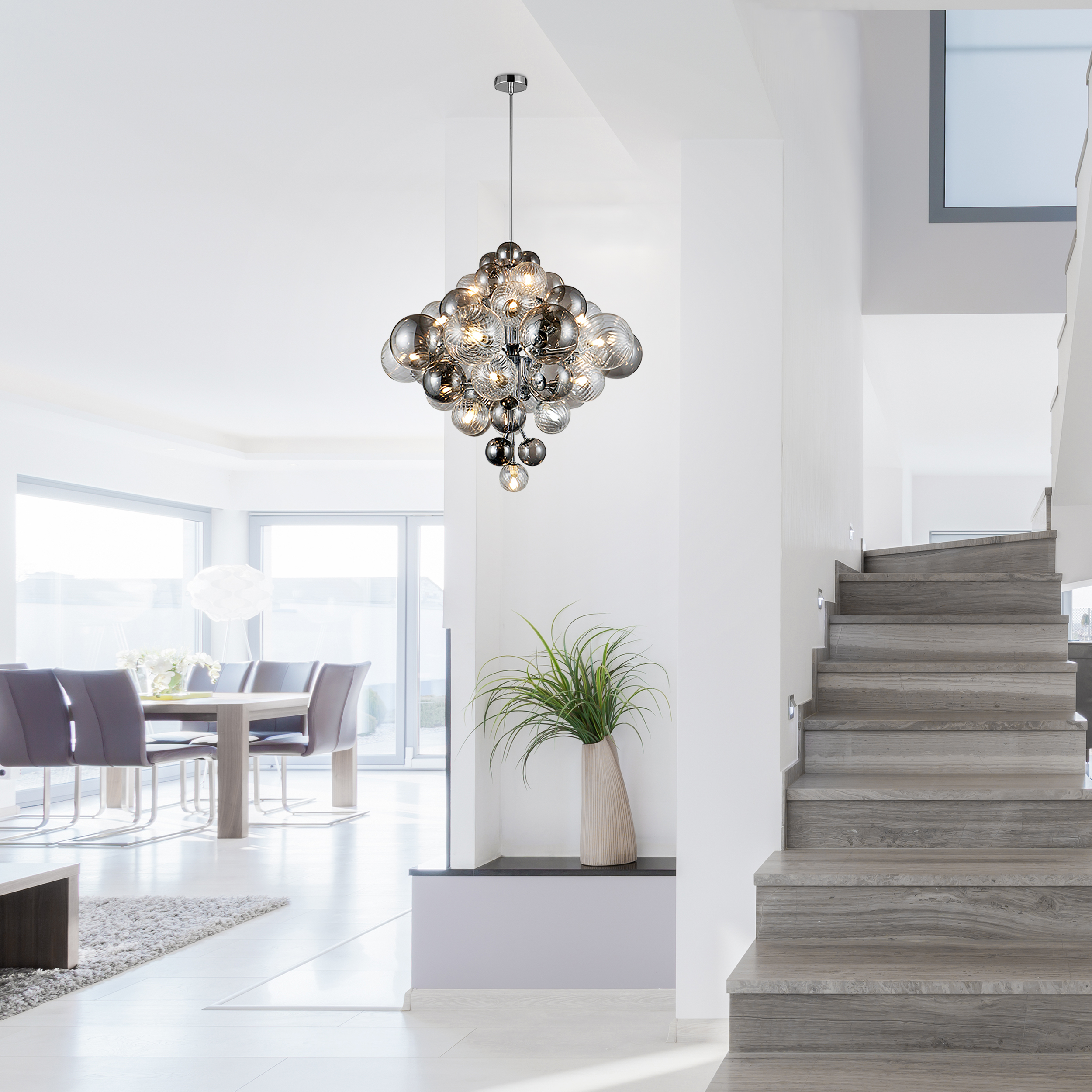 Ein modernes Interieur mit einem Kronleuchter. Treppe, eine Vase mit Pflanze und ein Esstisch im Hintergrund.