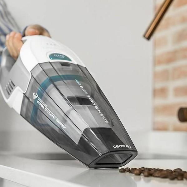 Un aspirapolvere portatile è tenuto da una persona. Chicchi di caffè e un rubinetto sullo sfondo.