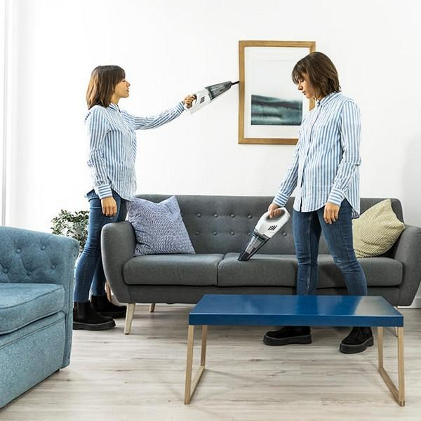 Due donne che puliscono un soggiorno con aspirapolvere portatili. Una aspira un muro, l'altra un divano.