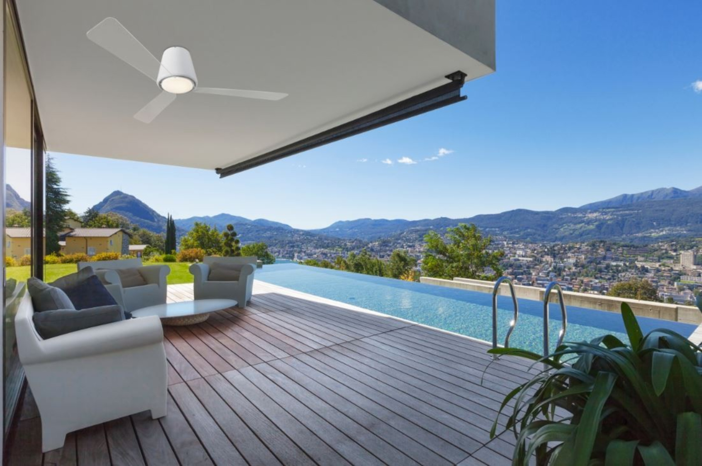 Ein moderner Außenbereich mit Pool, weißen Stühlen und einem Ventilator. Berge im Hintergrund.
