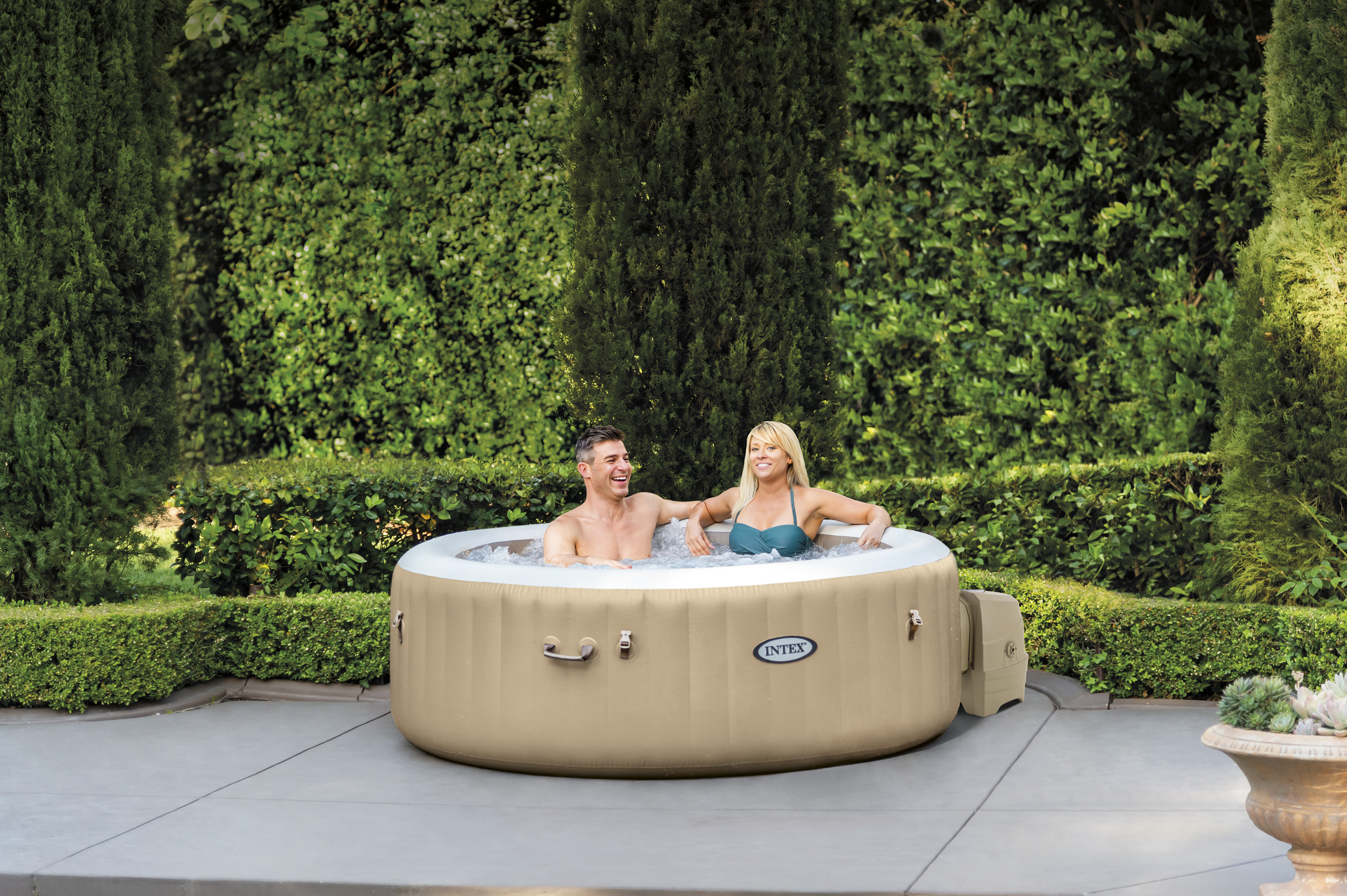 Ein Paar entspannt sich in einem aufblasbaren Whirlpool im Garten, umgeben von Grün.