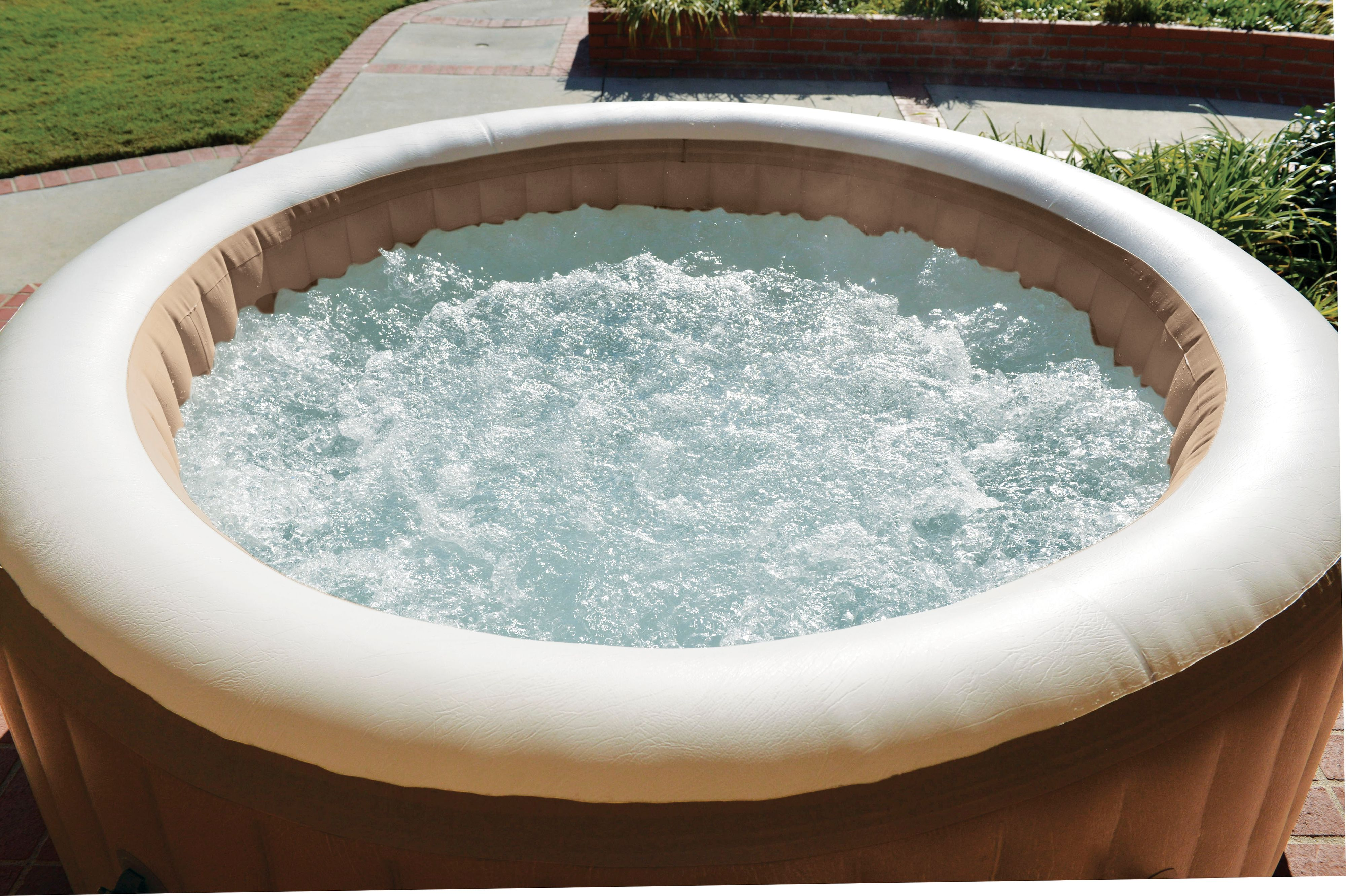 Runder aufblasbarer Whirlpool mit sprudelndem Wasser, im Freien auf einer Terrasse mit Bäumen.