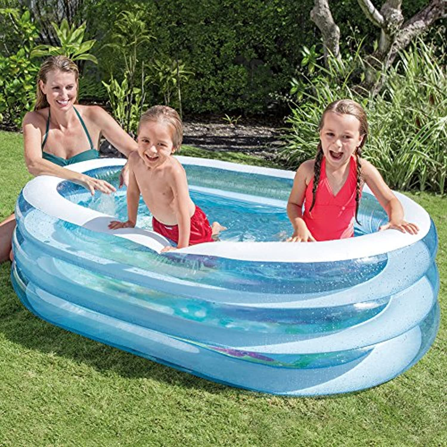 Drei Personen in einem aufblasbaren blauen Pool. Zwei Kinder spielen, ein Erwachsener lächelt.
