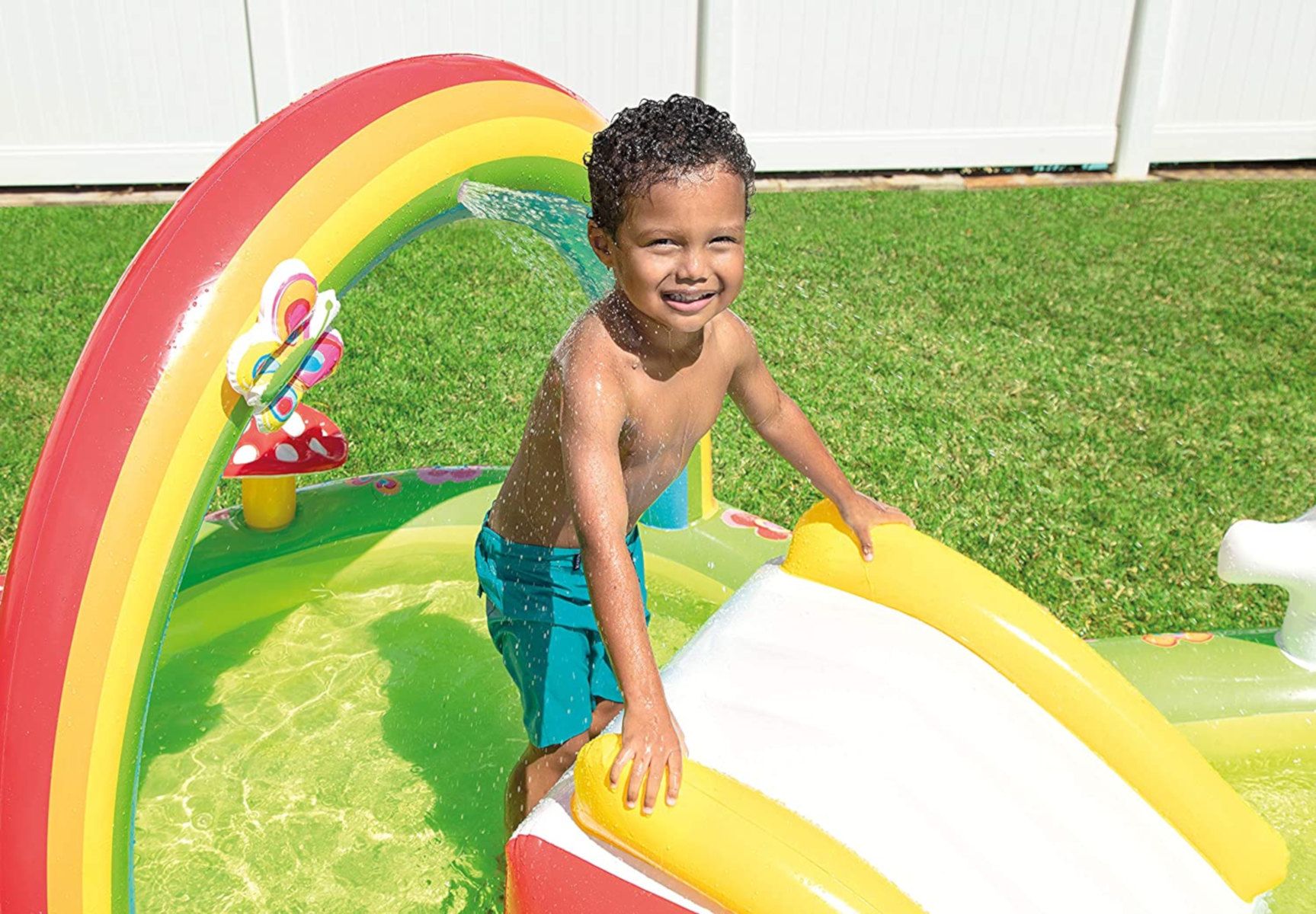 Un ragazzo in una piscina con un arco arcobaleno, sorridente e che guarda la fotocamera.