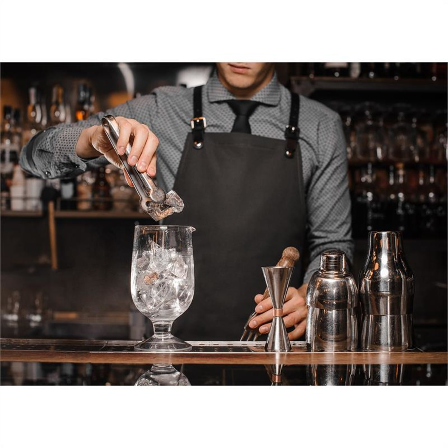 Barkeeper gibt Eis in ein Glas. Werkzeuge und Flaschen auf der Theke.