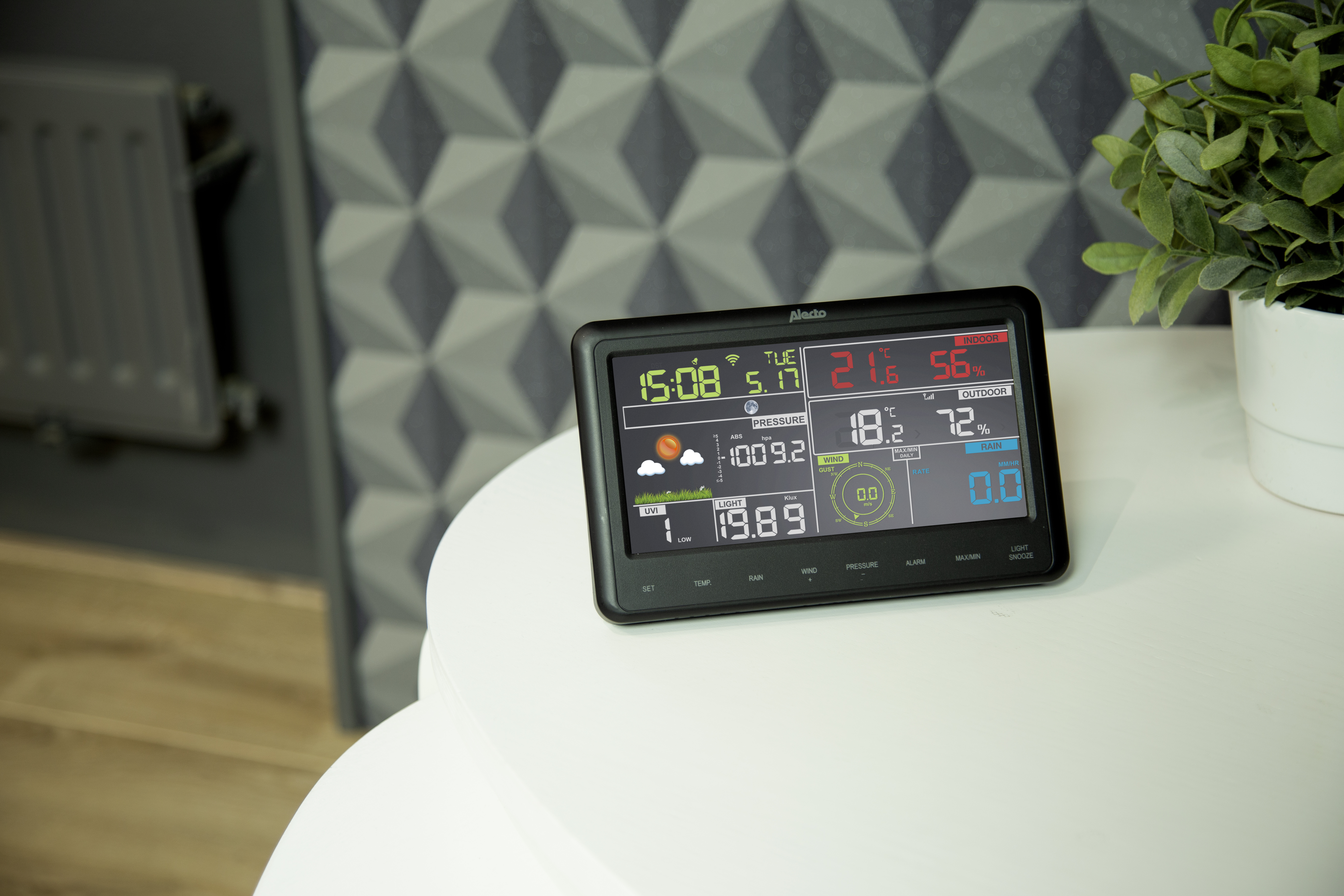 Een digitaal weerstation met diverse weergegevens. Geplaatst op een witte tafel.