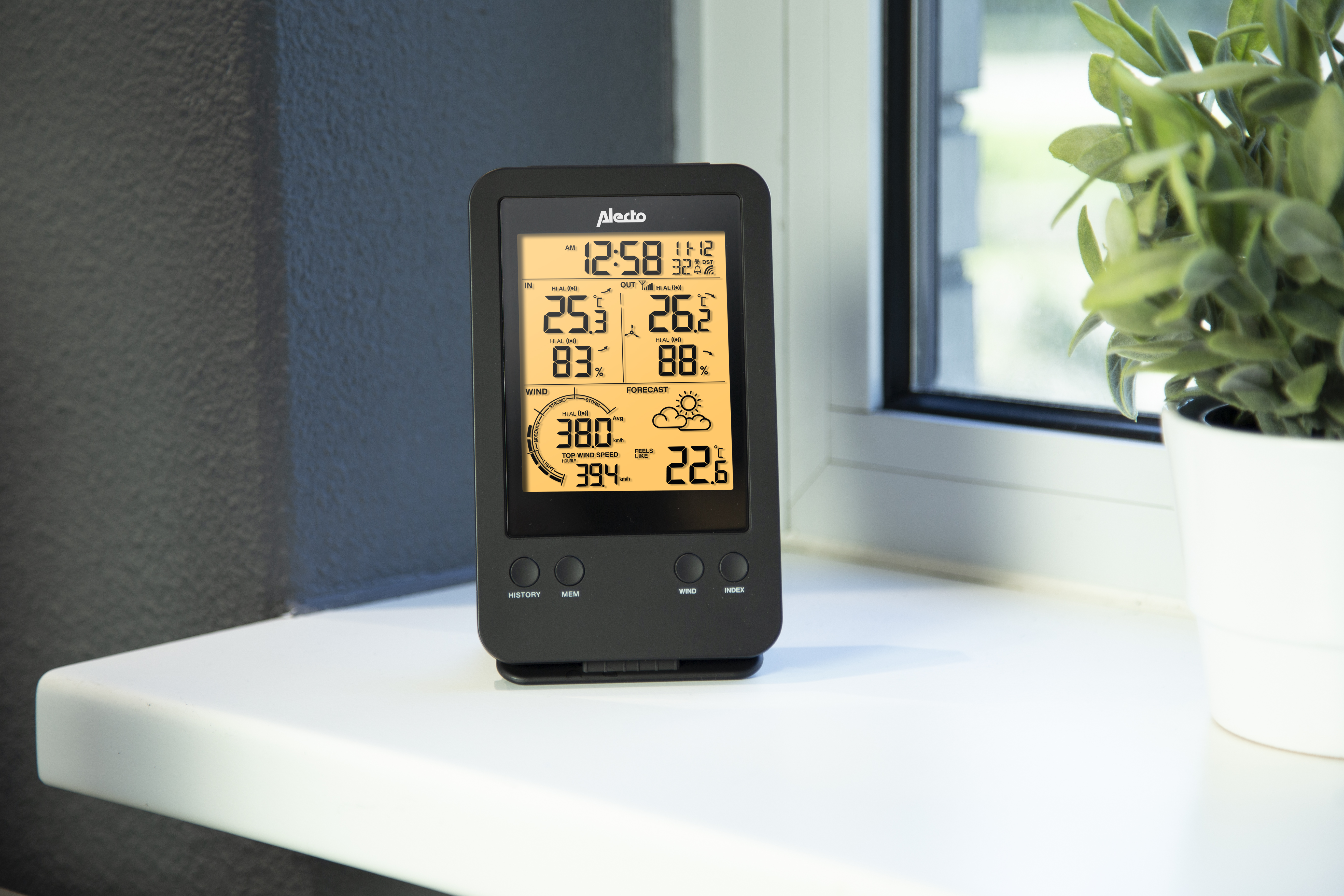 Czarna stacja pogodowa na białym parapecie. Wyświetla godzinę, temperaturę, wilgotność i prognozę.